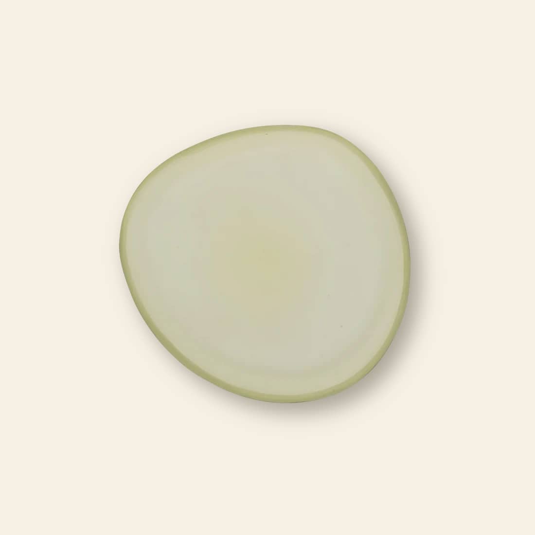 A single, irregularly shaped translucent onion slice rests on the Urban Nature Culture Plate Recycled Glass Frost by Urban Nature Culture, set against a plain, light beige background.