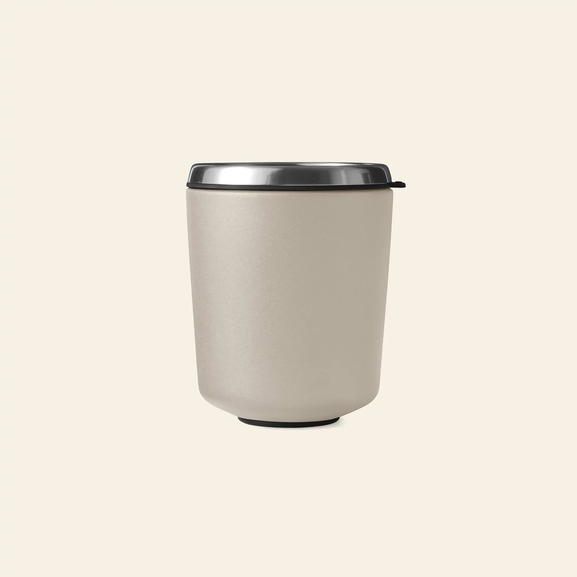The Vipp Vipp7 Toothbrush Holder by Vipp is a beige insulated travel mug with a black base and stainless steel lid, featuring a detachable rubber inner, perfect as a toothbrush holder or bathroom essential. Displayed on an off-white background.