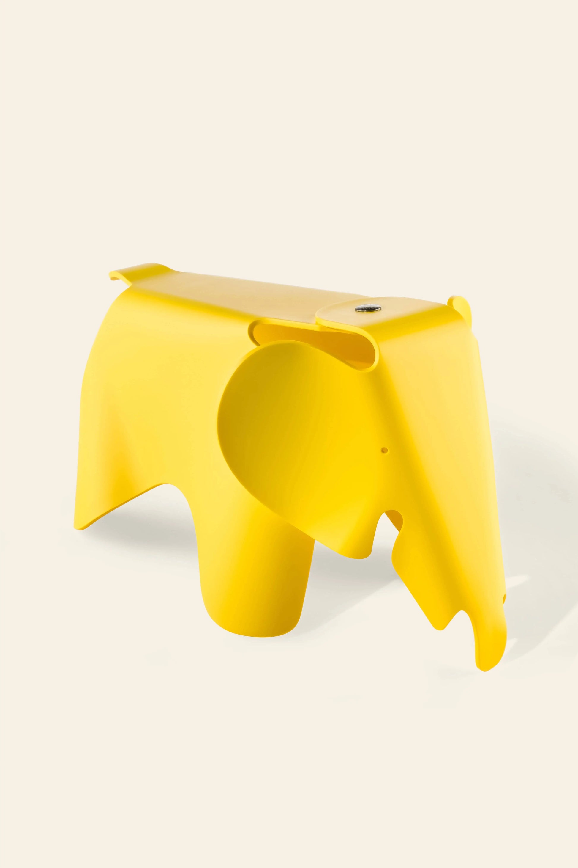 The Vitra Eames Elephant, Small by Vitra is a bright yellow, smooth plastic stool with stylized curves and simple features, adding a playful decorative touch against a plain light background.