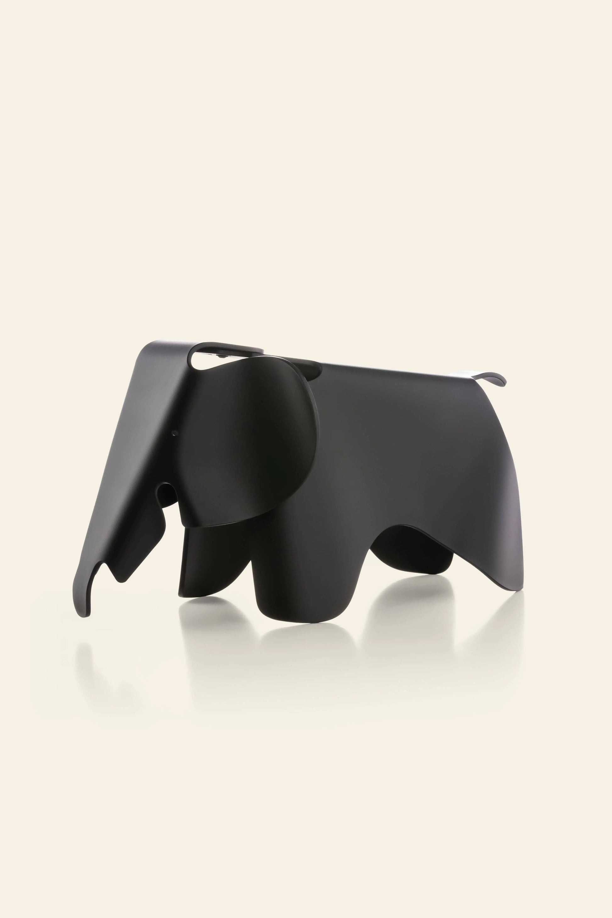 The Vitra Eames Elephant, Small by Vitra is a black, minimalist figurine with smooth curves, displayed against a light beige background. This iconic modern piece adds an abstract and decorative touch to any space.