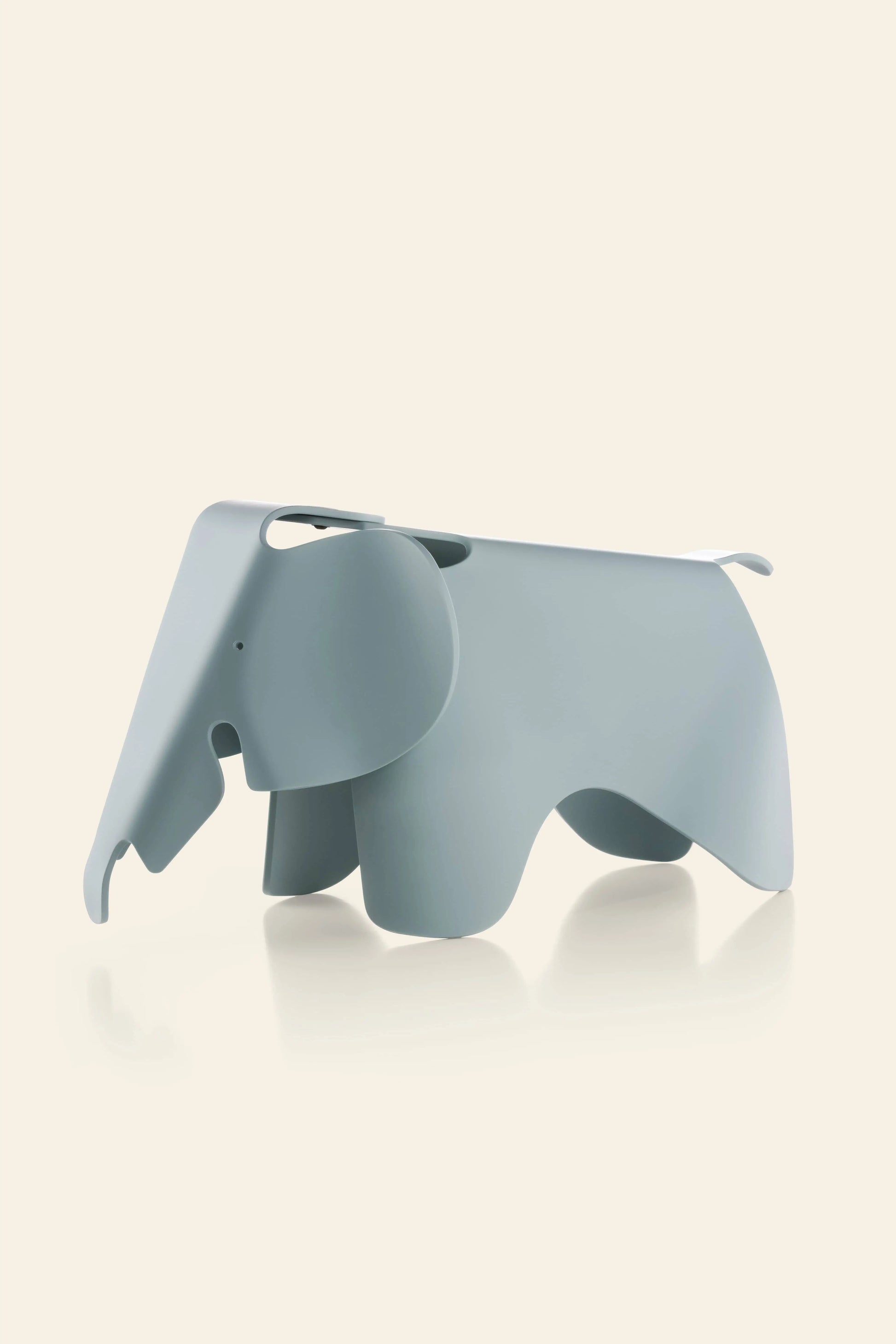 A minimalist Vitra Eames Elephant, Small by Vitra in light gray stands on a plain beige background. Its smooth, curved form features abstract cutouts outlining the legs, ears, and trunk for a refined decorative accent.