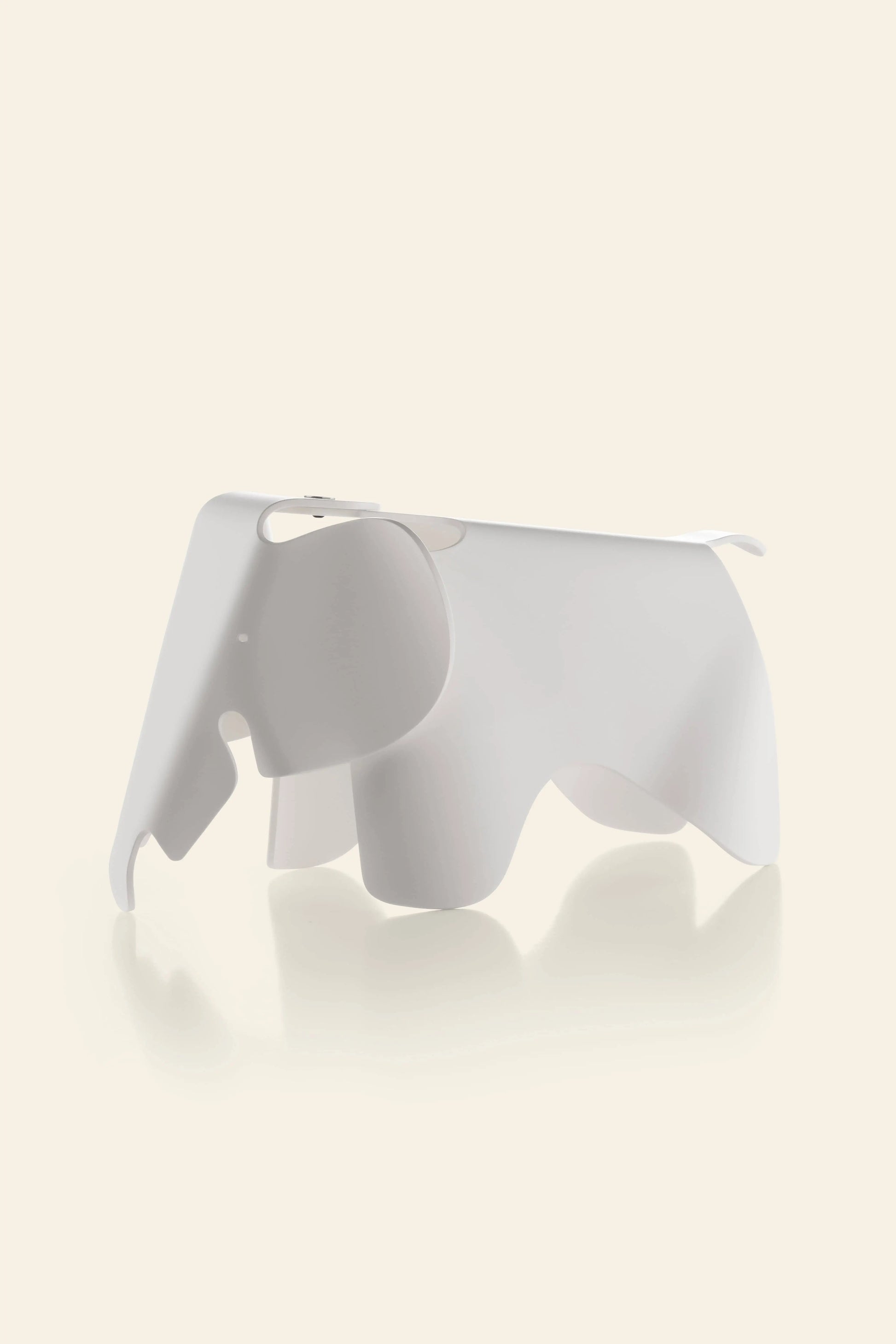 The Vitra Eames Elephant, Small by Vitra is a minimalist, white, abstract decorative piece with a smooth finish, shaped like an elephant and set against a light beige background with a gentle reflection beneath it.