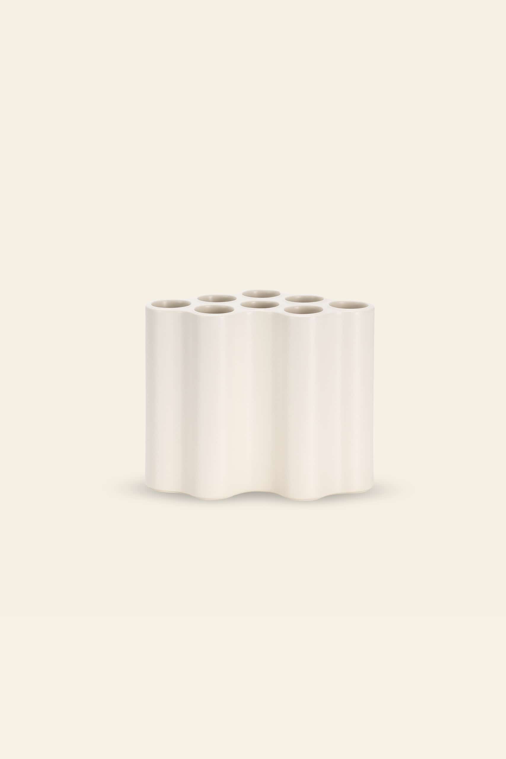 The Vitra Nuage Ceramique, Medium by Vitra is a minimalist off-white ceramic vase featuring six circular top openings and a wavy form, displayed against a plain beige background.