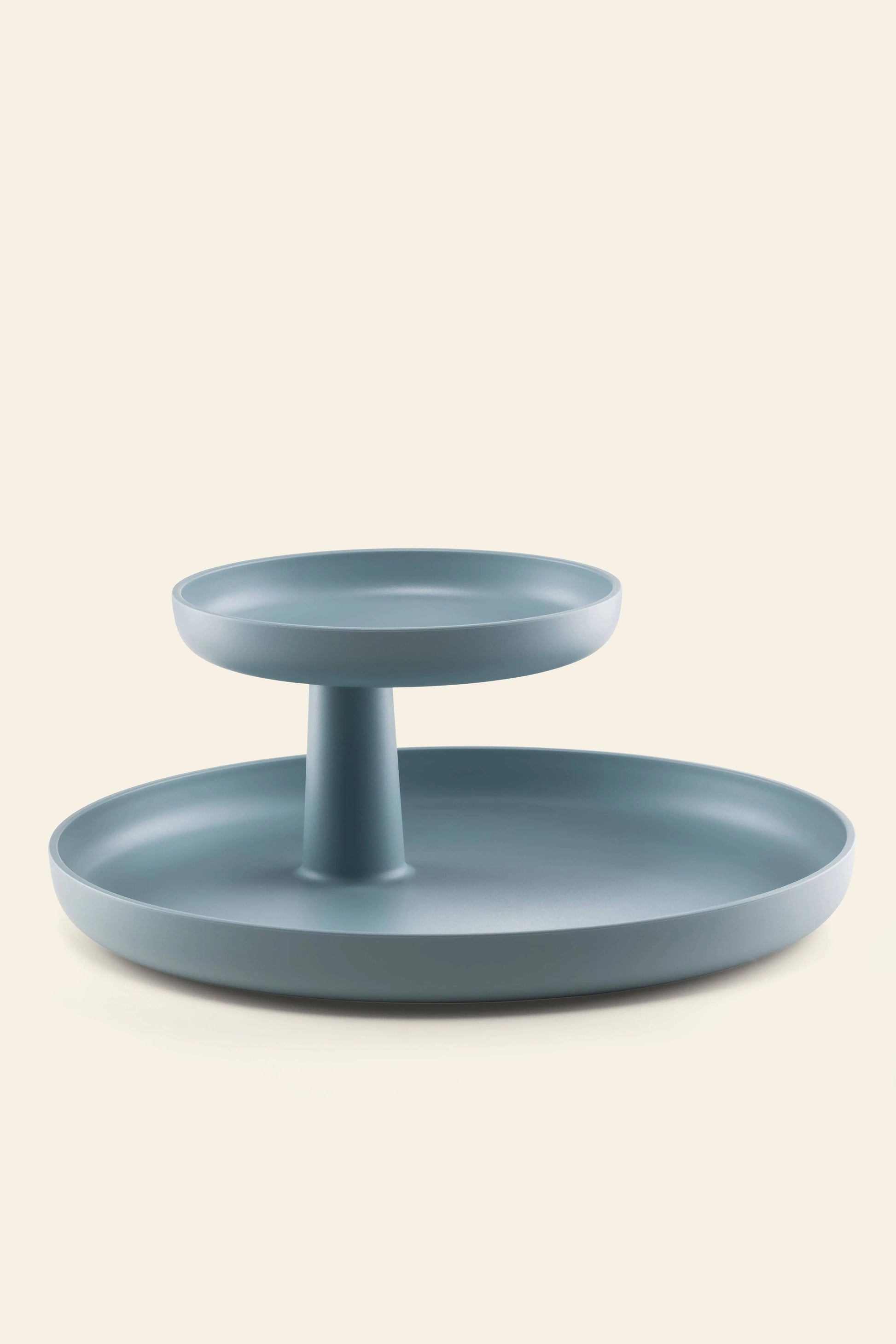 The Vitra Rotary Tray by Vitra features a modern, two-tiered design in light blue, with a smaller top tray elevated above the larger bottom tray by a central column, shown against an off-white background.