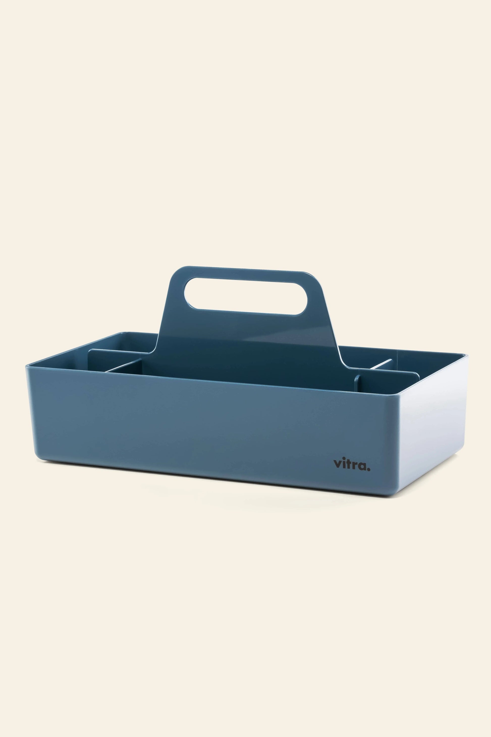 A blue rectangular Vitra Toolbox RE by Vitra, made from recycled ABS with a central handle and internal dividers, features “vitra.” on the front corner and is set against a plain light background.
