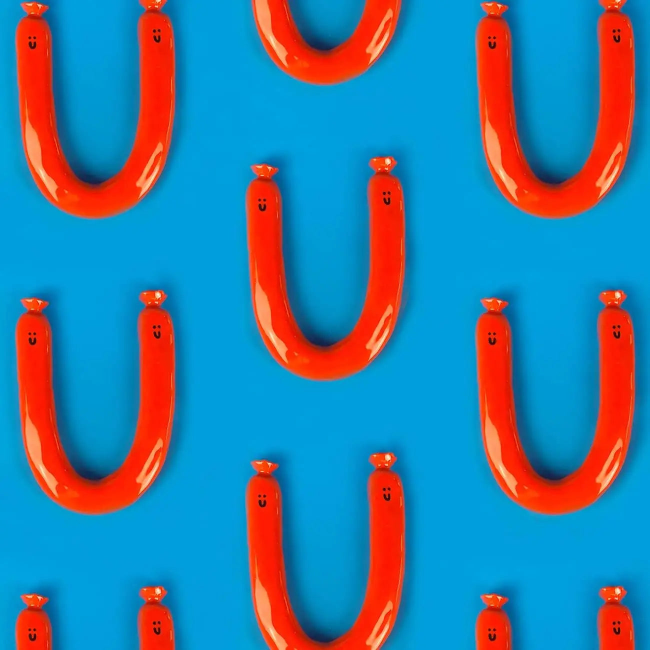 Wobbly Studio Happy Saucisse Wall Decor features red, U-shaped sausages with smiling faces on a bright blue background—unique handcrafted wall art by Wobbly Studio to brighten any room.