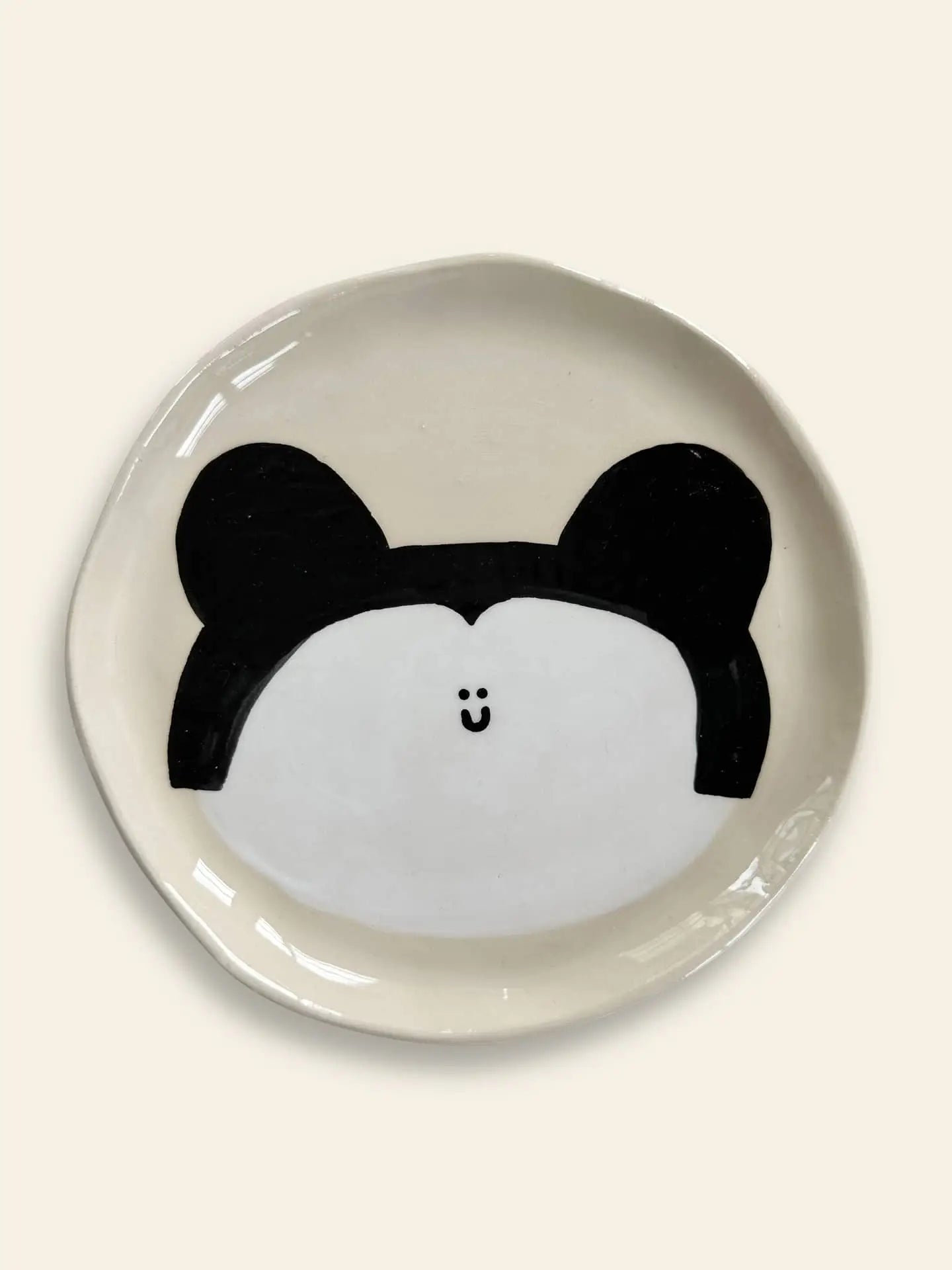 The Wobbly Studio Happy Things Plate - Souris is a cream-colored ceramic plate with a simple round animal face, black ears, and a small smiling mouth, from Wobbly Studios Happy Things collection.