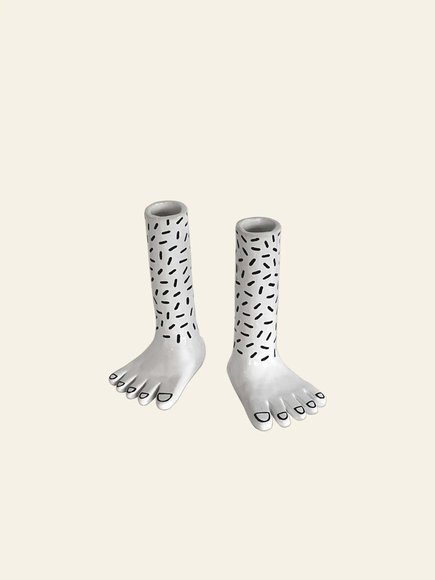 Wobbly Studio Pair Of Legs Vase: Two ceramic foot-shaped vases by Wobbly Studio, featuring black abstract patterns on the legs and black lines on the toenails, displayed against a plain beige background.