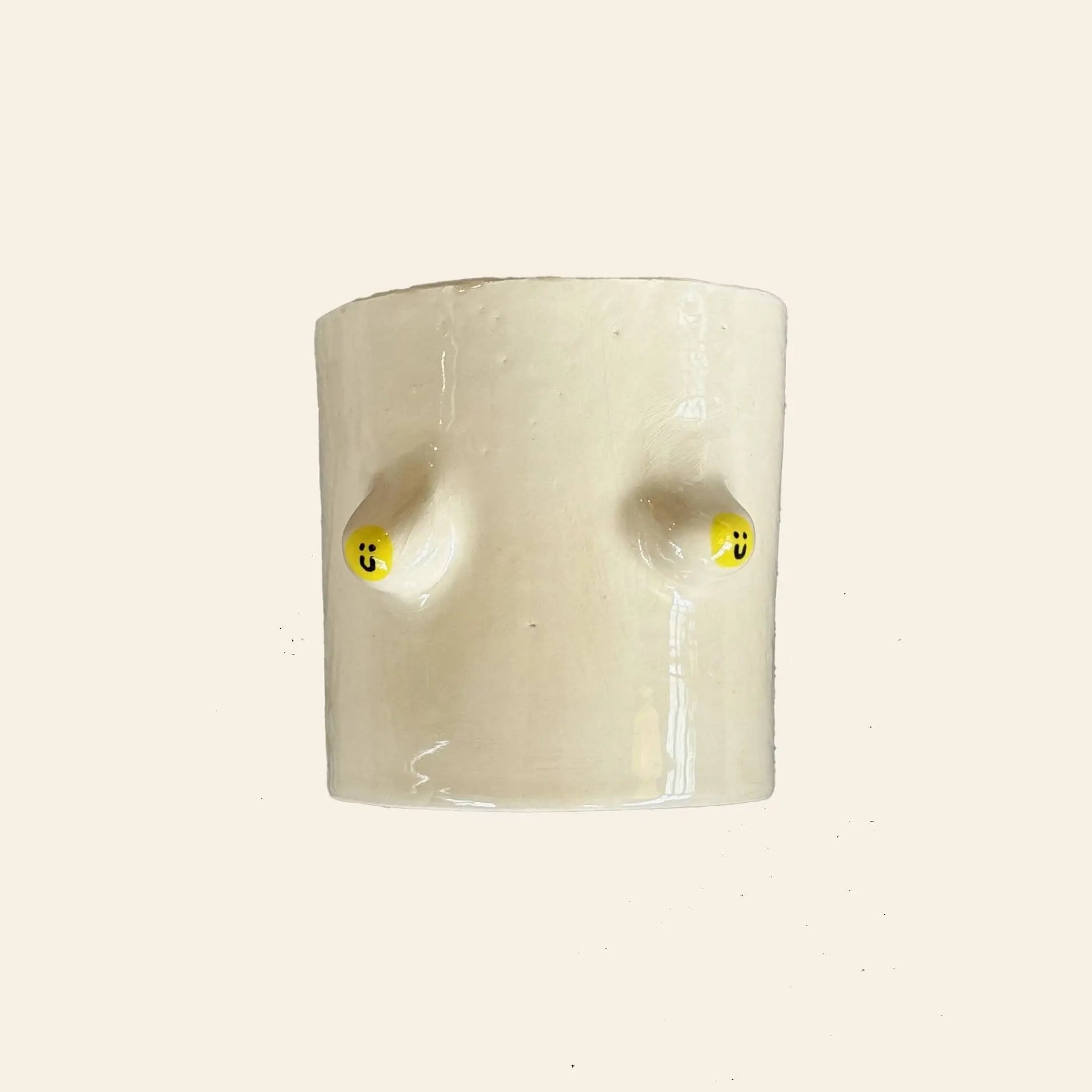 The Wobbly Studio Regular Boobies Pot is a cream-colored ceramic planter featuring two front protrusions, each topped with a yellow smiley face, shown against a plain light background.
