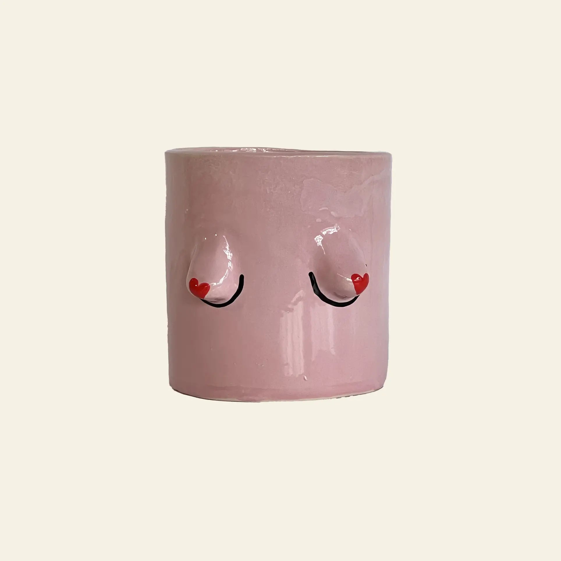 The Wobbly Studio Regular Boobies Pot is a pink handcrafted cylindrical planter with two raised nipple-like shapes, black curved lines, and small red hearts—a playful decor piece for any space by Wobbly Studio.