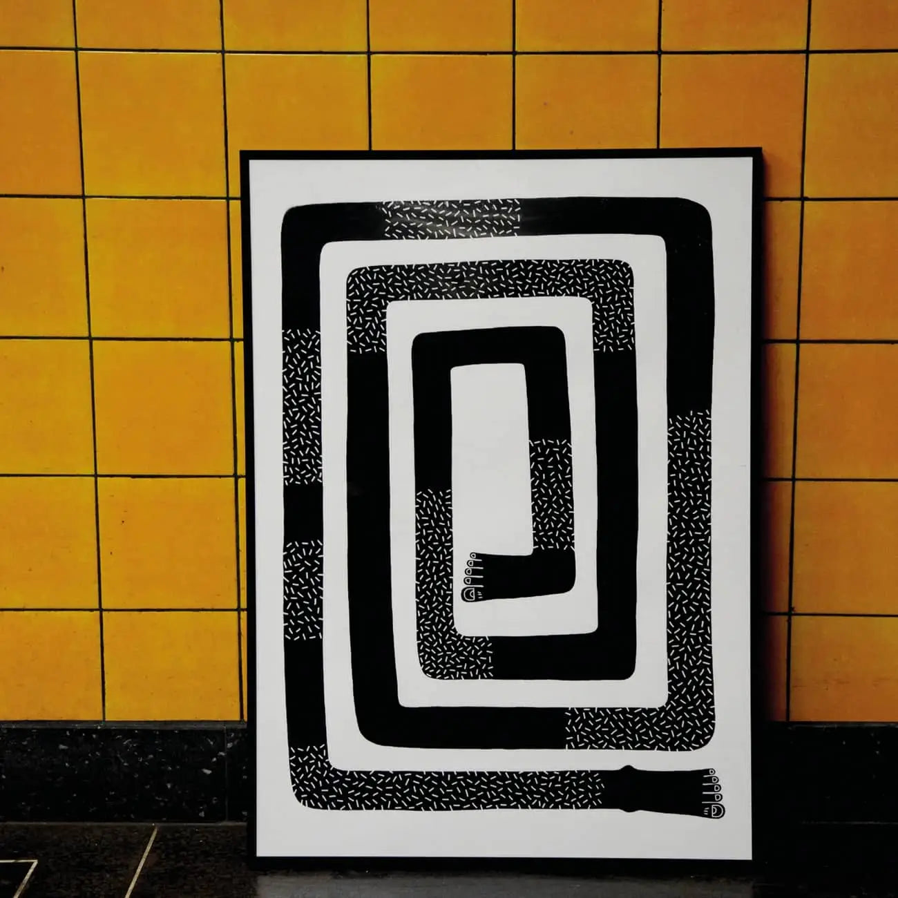 Wobbly Studio The Maze (50x70) by Wobbly Studio is a signed and numbered artwork with a black zigzagging spiral design featuring hand shapes at the ends, set against a yellow tiled wall.