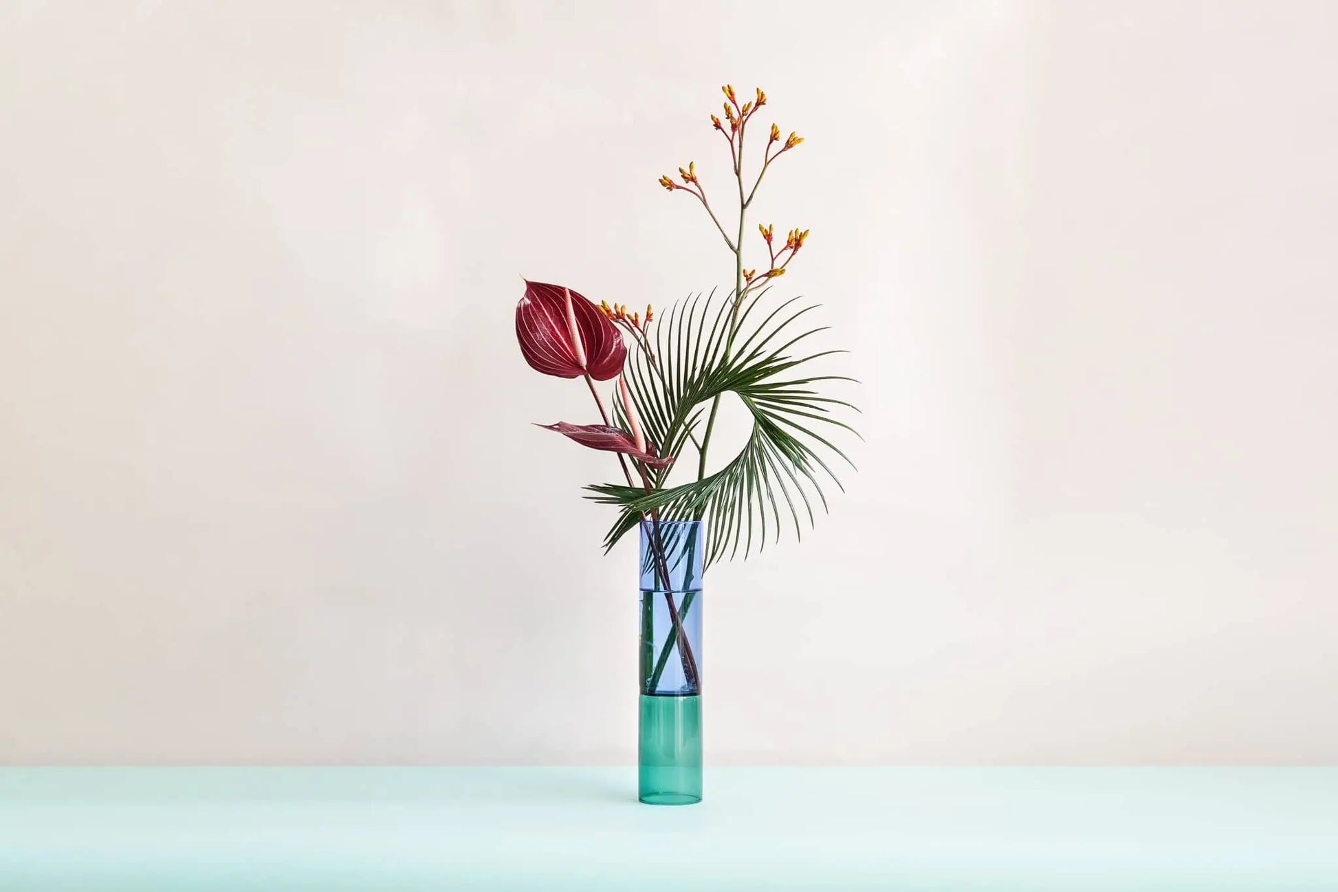 The Wonderland Botanicals Bamboo Groove Vase Arrangement features a minimalist Anthurium design with tropical leaves and colorful foliage in a tall handmade glass vase by Wonderland Botanicals.
