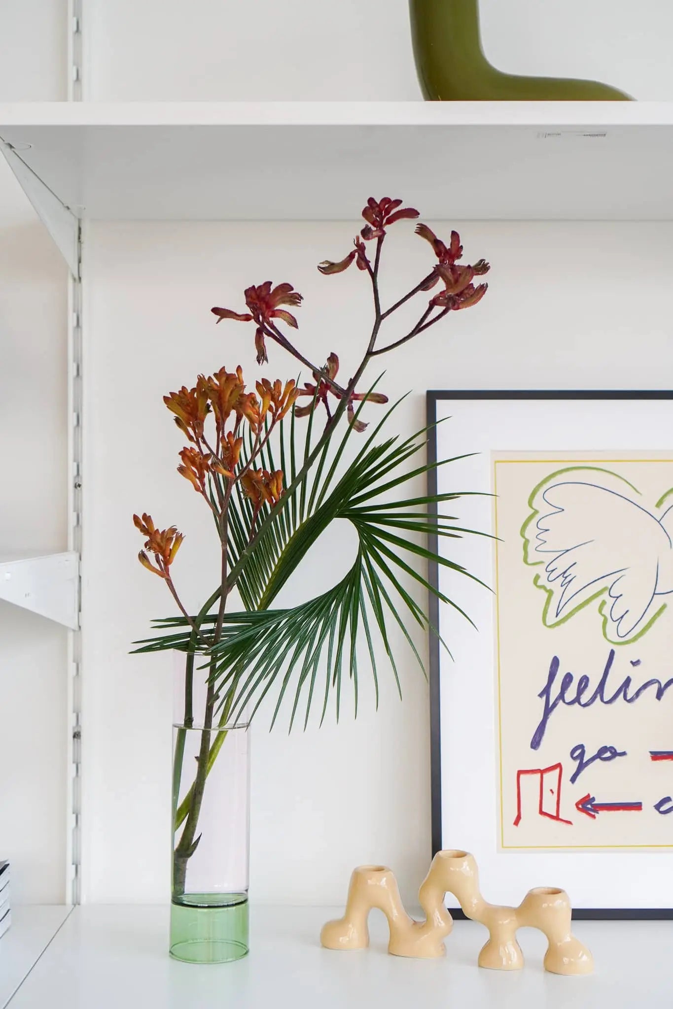The Wonderland Botanicals Bamboo Groove Vase Arrangement adds floral texture to your home decor, displayed with a framed abstract artwork and a beige ceramic piece shaped like four arches.