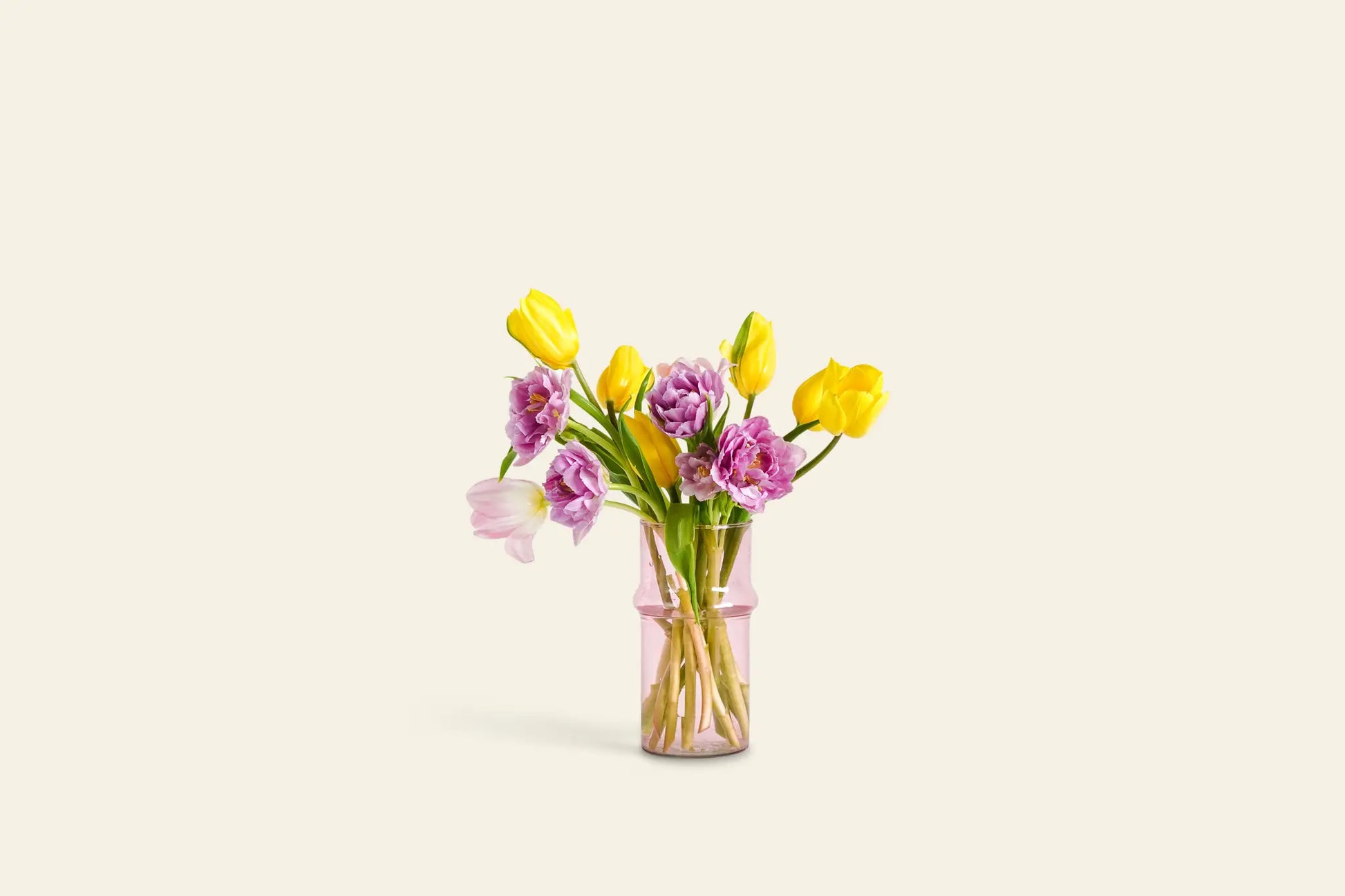 The Rosé vase by Wonderland Botanicals holds yellow tulips and purple flowers, elegantly centered against a light beige background—an ideal accent for any home decor.