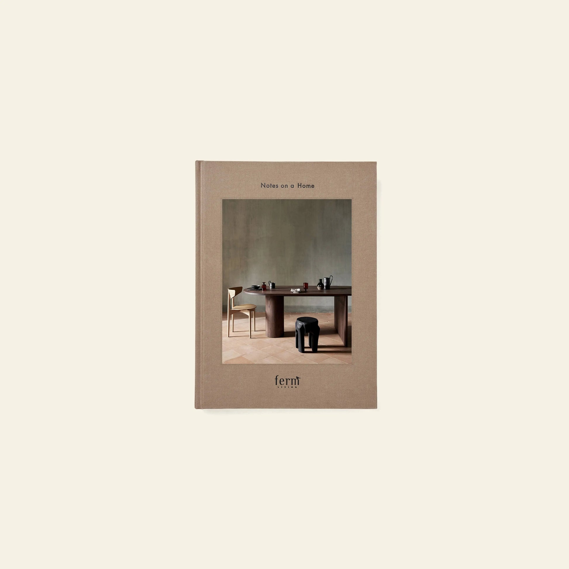 The ferm LIVING Coffee Table Book 2023 is a beige hardcover book featuring a minimalist interior with a wooden table, chairs, ceramics, and decor on the cover—reflecting ferm LIVING’s design concept against a plain light background.