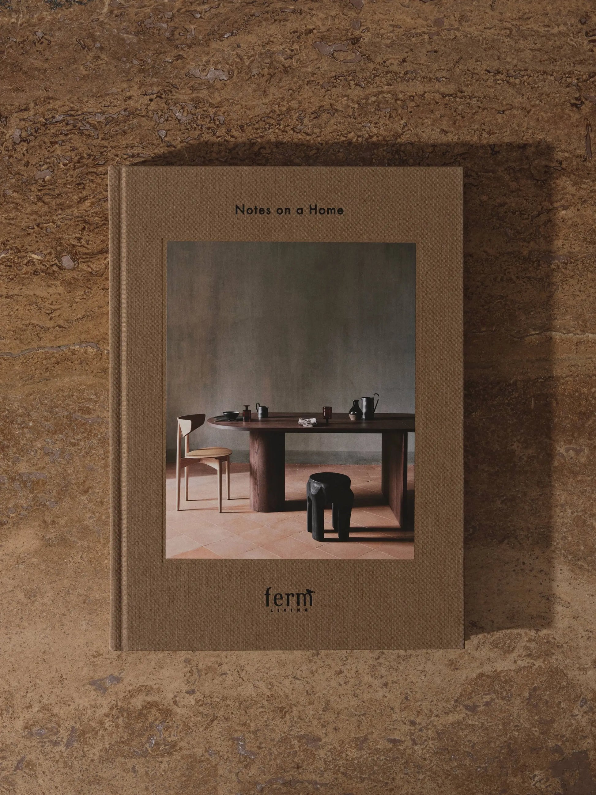 The ferm LIVING Coffee Table Book 2023 is a brown hardcover featuring a minimalist dining table and chairs on the cover, echoing ferm LIVING’s design philosophy and creative vision.