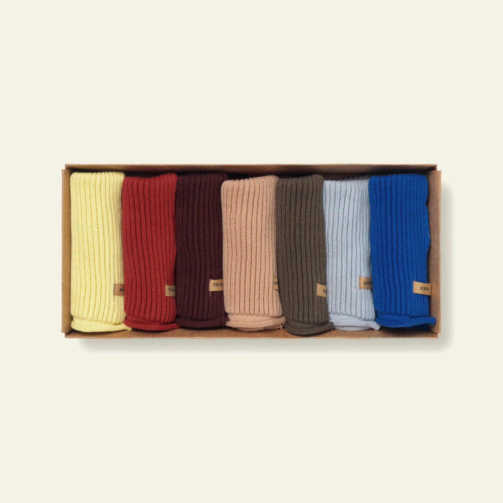 A rectangular box containing seven ferm LIVING Day Cloths—each crafted from soft organic cotton in assorted colors and finished with a small brown tag.