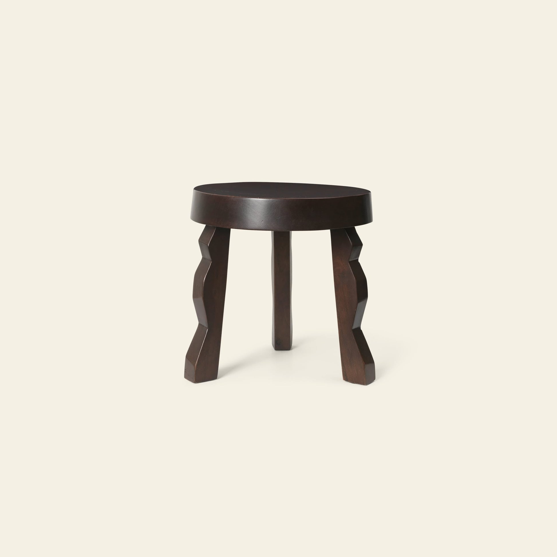 The ferm LIVING Faye Stool, crafted from FSC-certified mango wood with a round seat and three zigzag legs, makes a striking accent against a plain, light background.