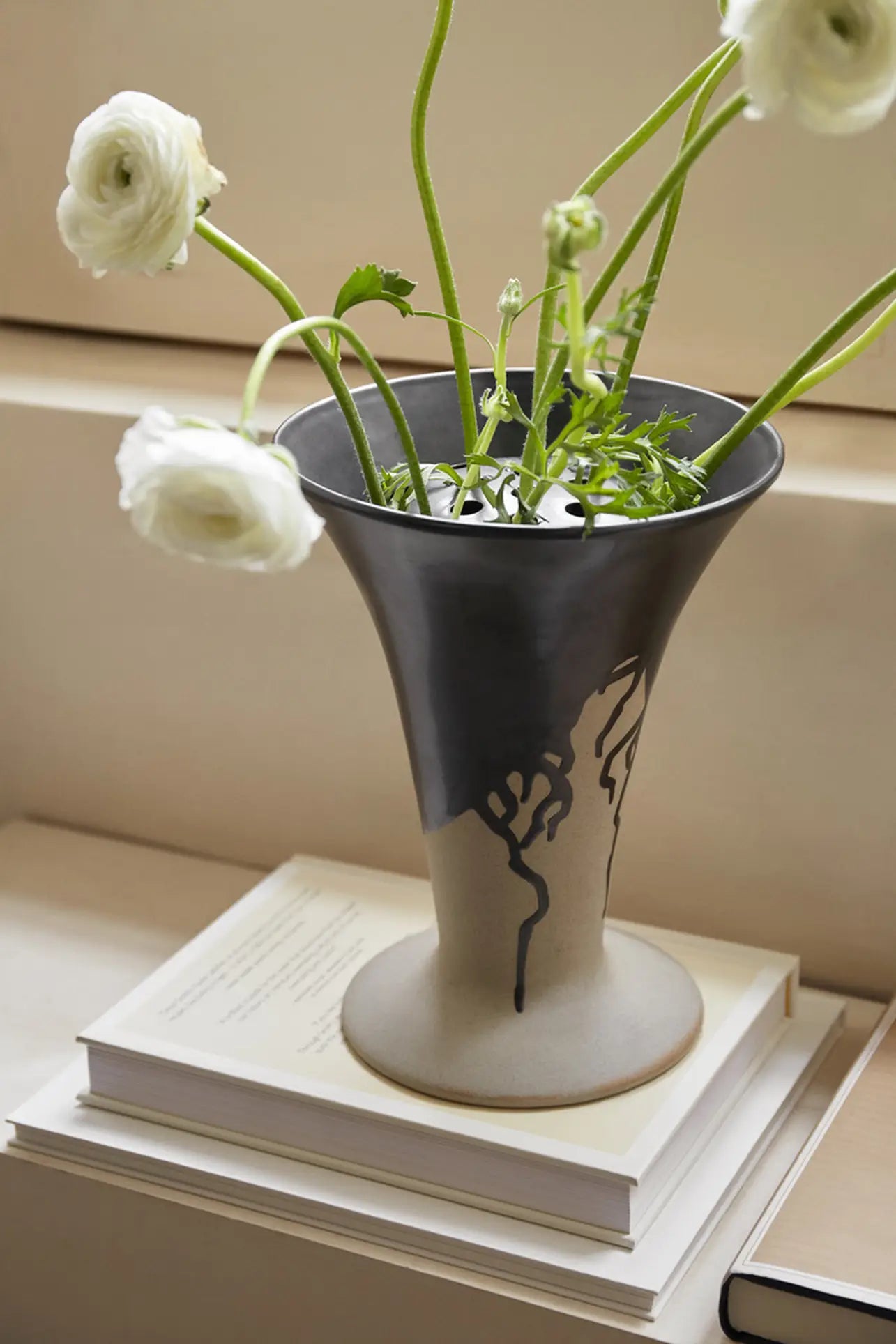 The ferm LIVING Flores Vase by ferm LIVING, featuring a black and beige abstract pattern, holds white flowers with green stems and is displayed on two stacked books on a light surface.