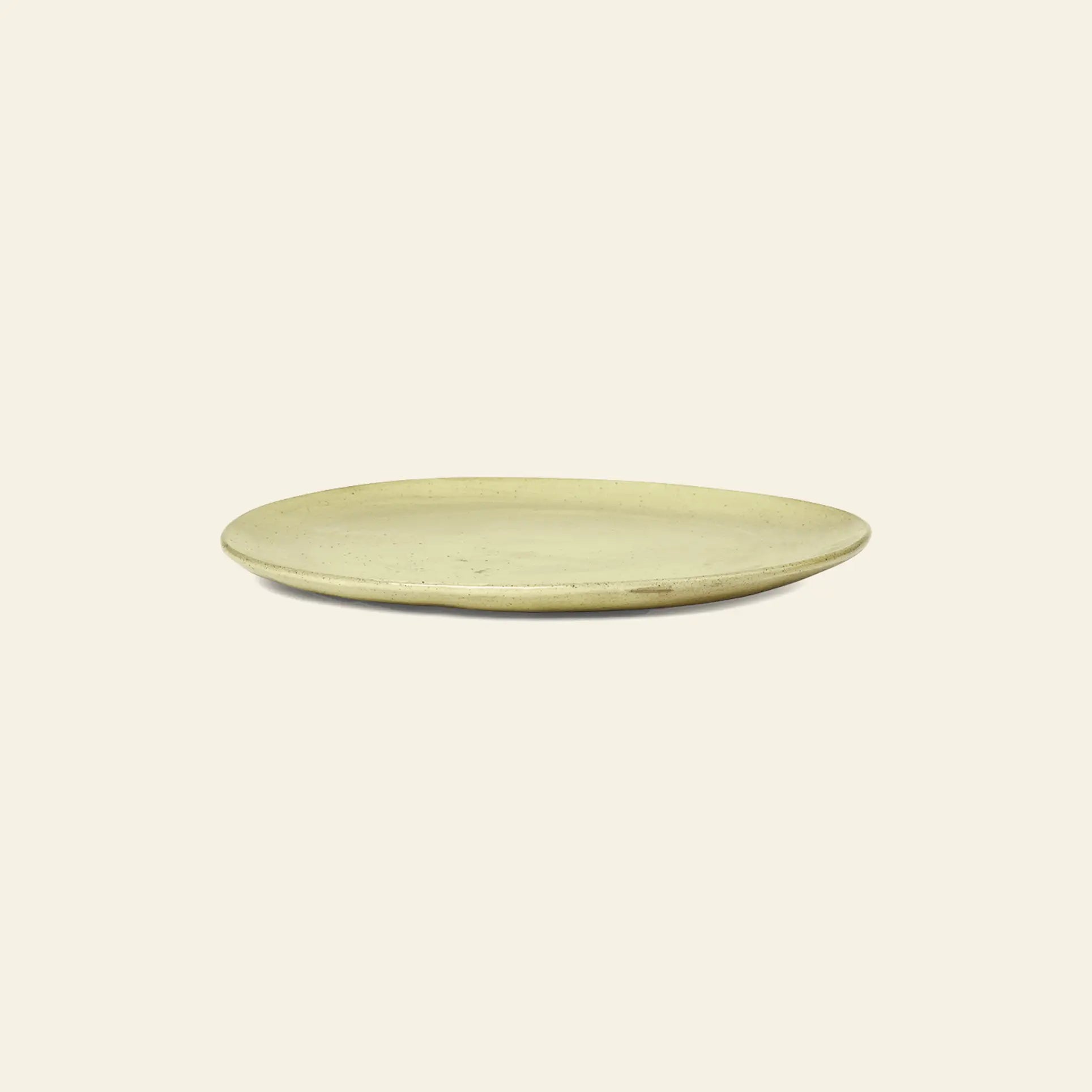 The ferm LIVING Flow Plate, Medium is a simple round beige ceramic plate with a semi-matte glaze and slightly irregular edge, designed by ferm LIVING and shown on a plain light background.