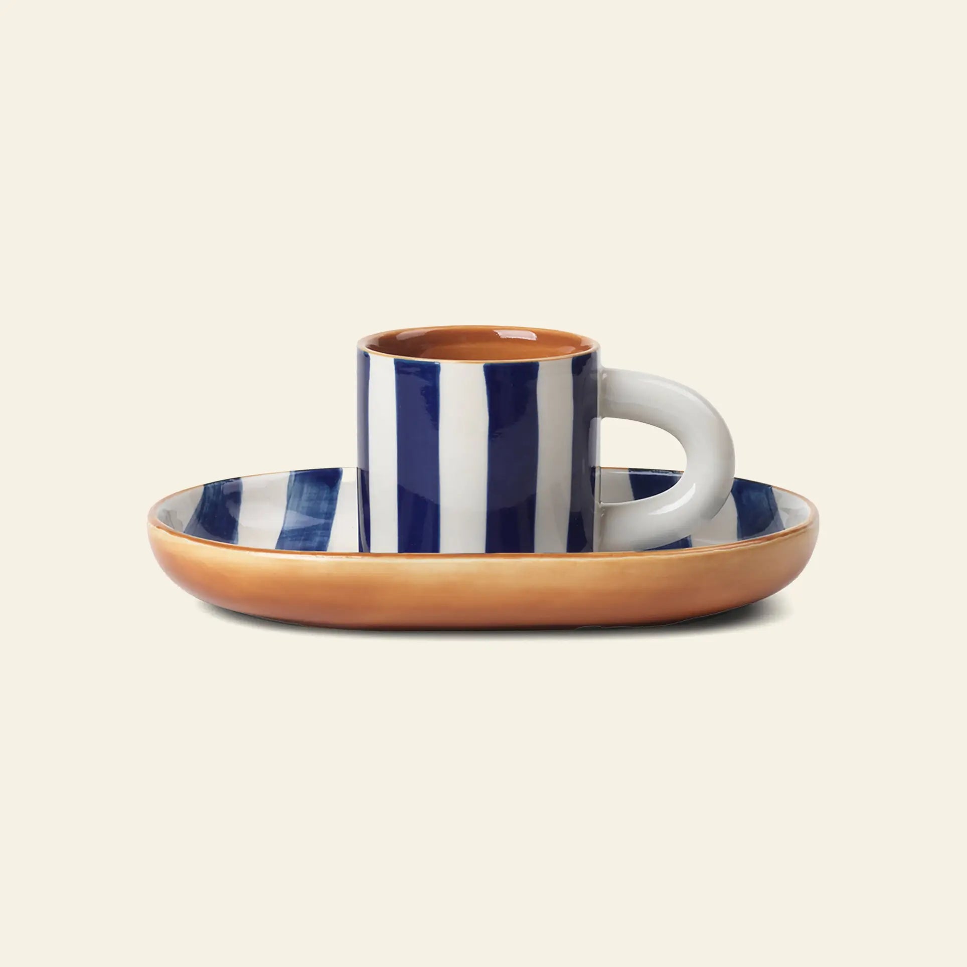 A hand-painted blue and white ceramic espresso cup rests on an oval saucer with a brown rim, displayed against a beige background—part of the ferm LIVING Milu Snack Set, crafted from glazed stoneware by ferm LIVING.