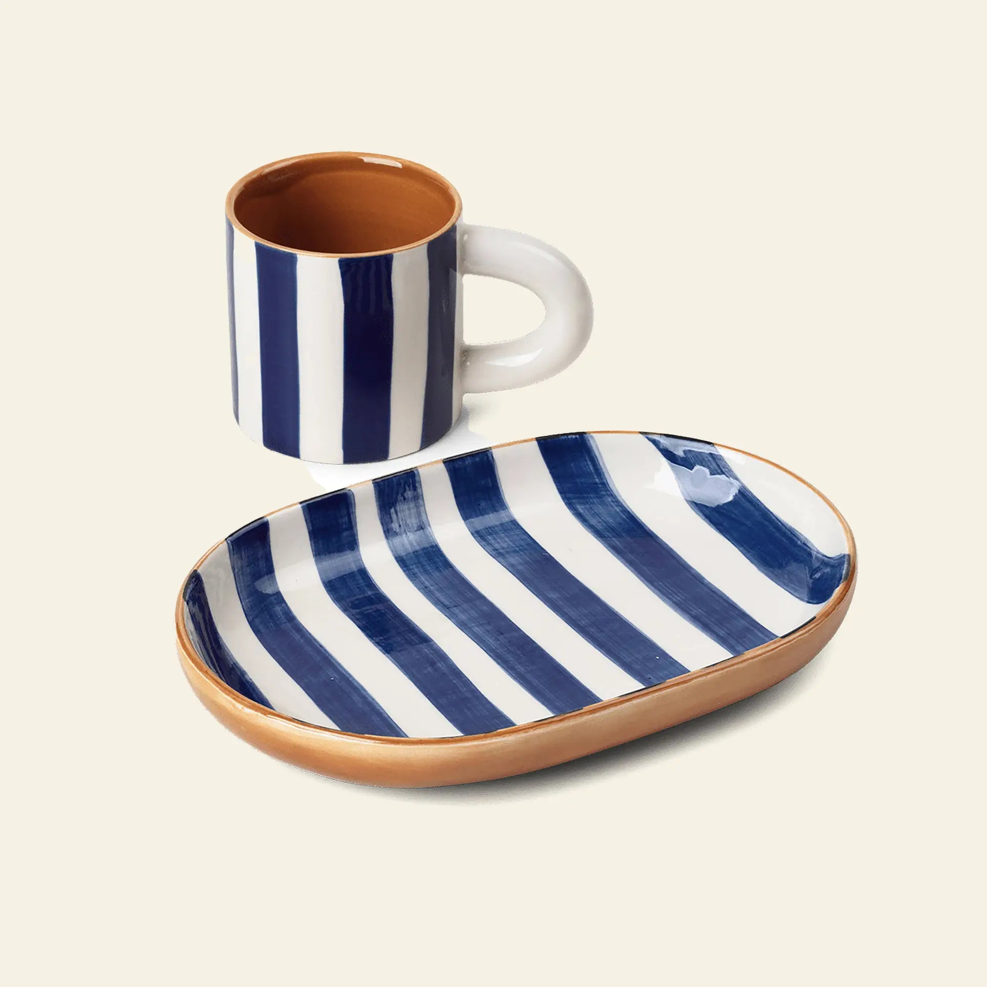 The ferm LIVING Milu Snack Set includes a ceramic mug and oval plate made from glazed stoneware, decorated with hand-painted blue and white stripes and tan edges on a light background.