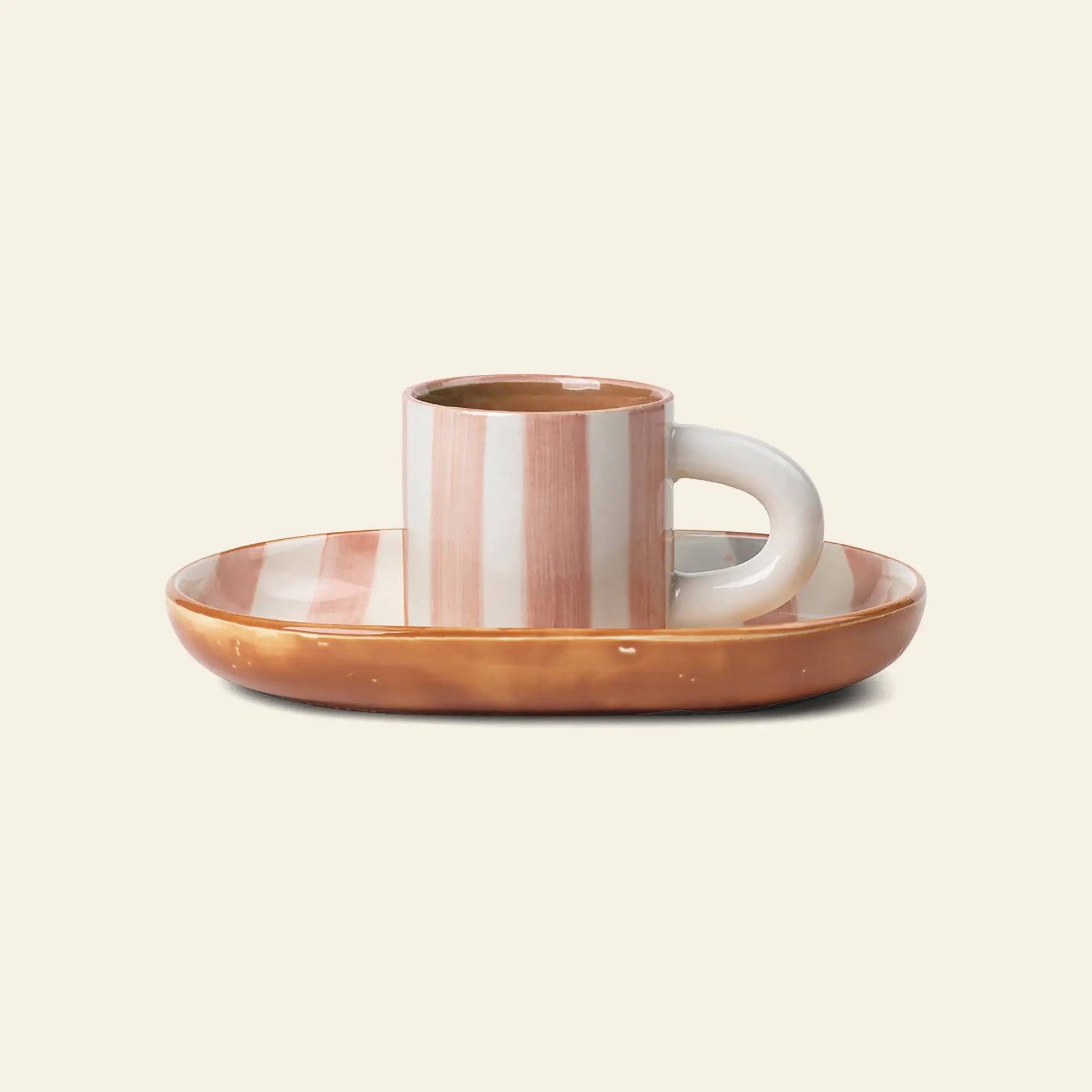 A ferm LIVING Milu Snack Set ceramic mug with hand-painted vertical beige and white stripes rests on an oval, glossy tan-brown saucer. The set by ferm LIVING is displayed against a light cream background.