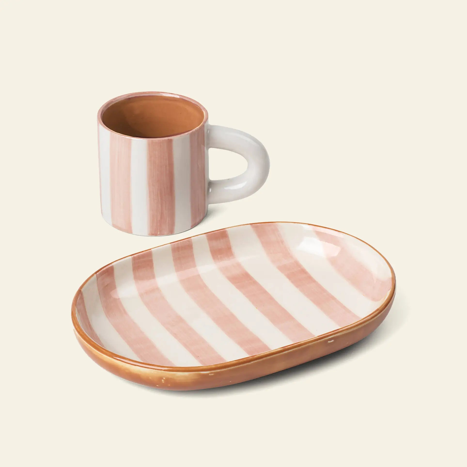 The ferm LIVING Milu Snack Set includes a ceramic mug and plate with pink and white hand-painted stripes on a cream background, both featuring a glossy stoneware finish and modern design.
