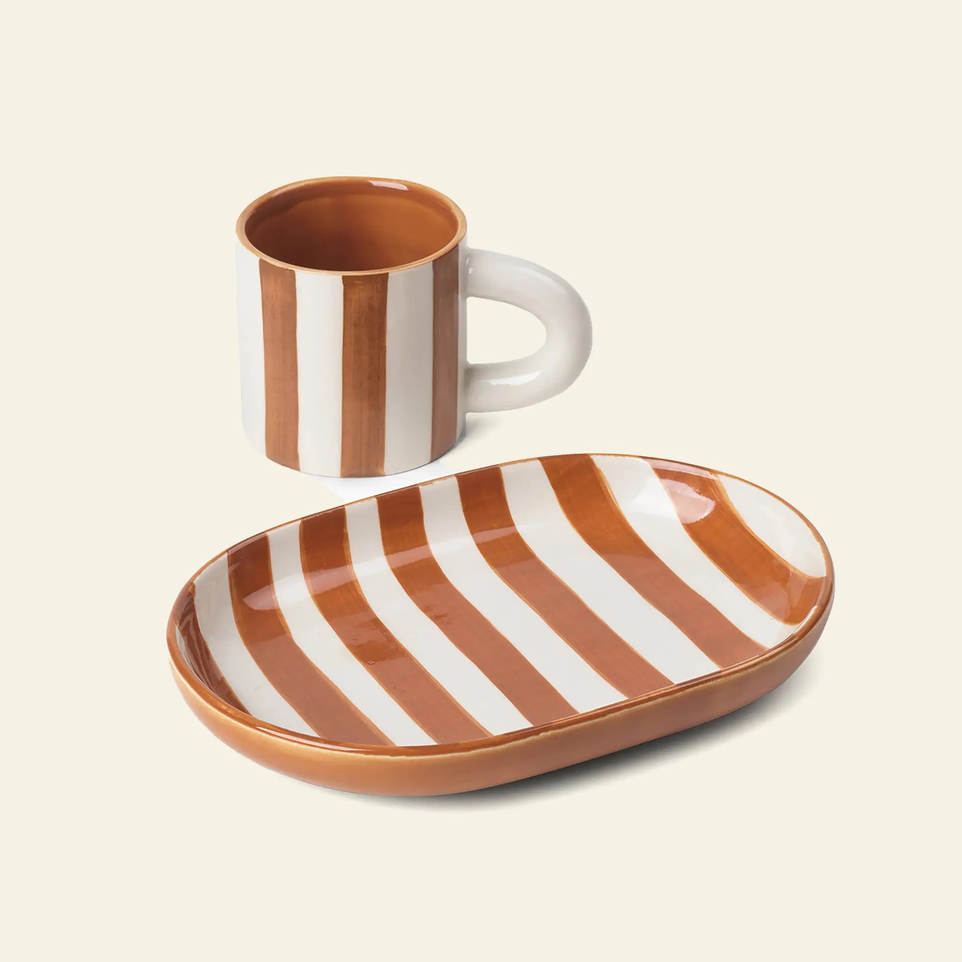 The ferm LIVING Milu Snack Set features a ceramic mug and oval plate made from glazed stoneware, both hand-painted with vertical brown and white stripes on a light background.