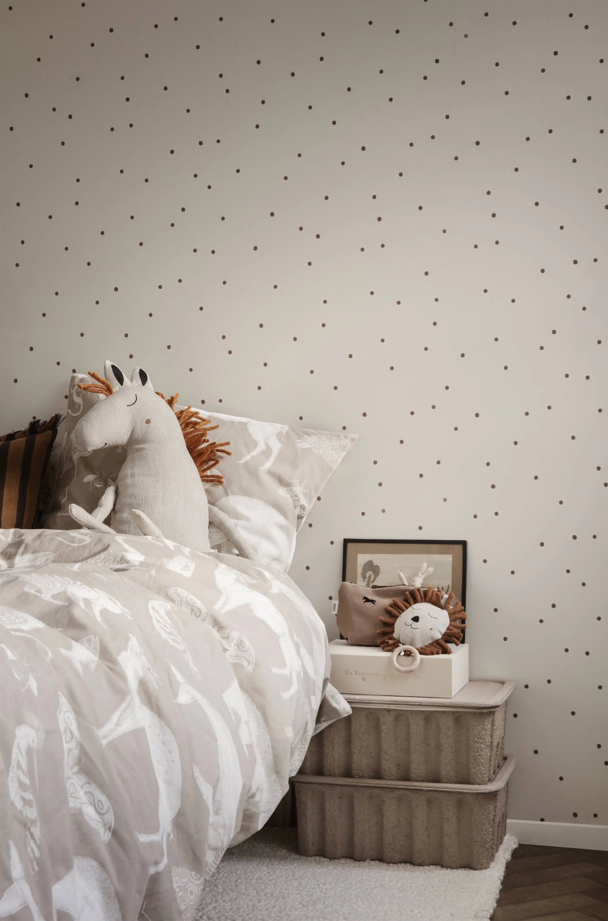 A cozy children’s bedroom with beige bedding, plush horse and lion toys, and two ferm LIVING Paper Pulp Box Large sets topped with framed art, a cup, and a small lion toy. The wall has a playful polka dot pattern.