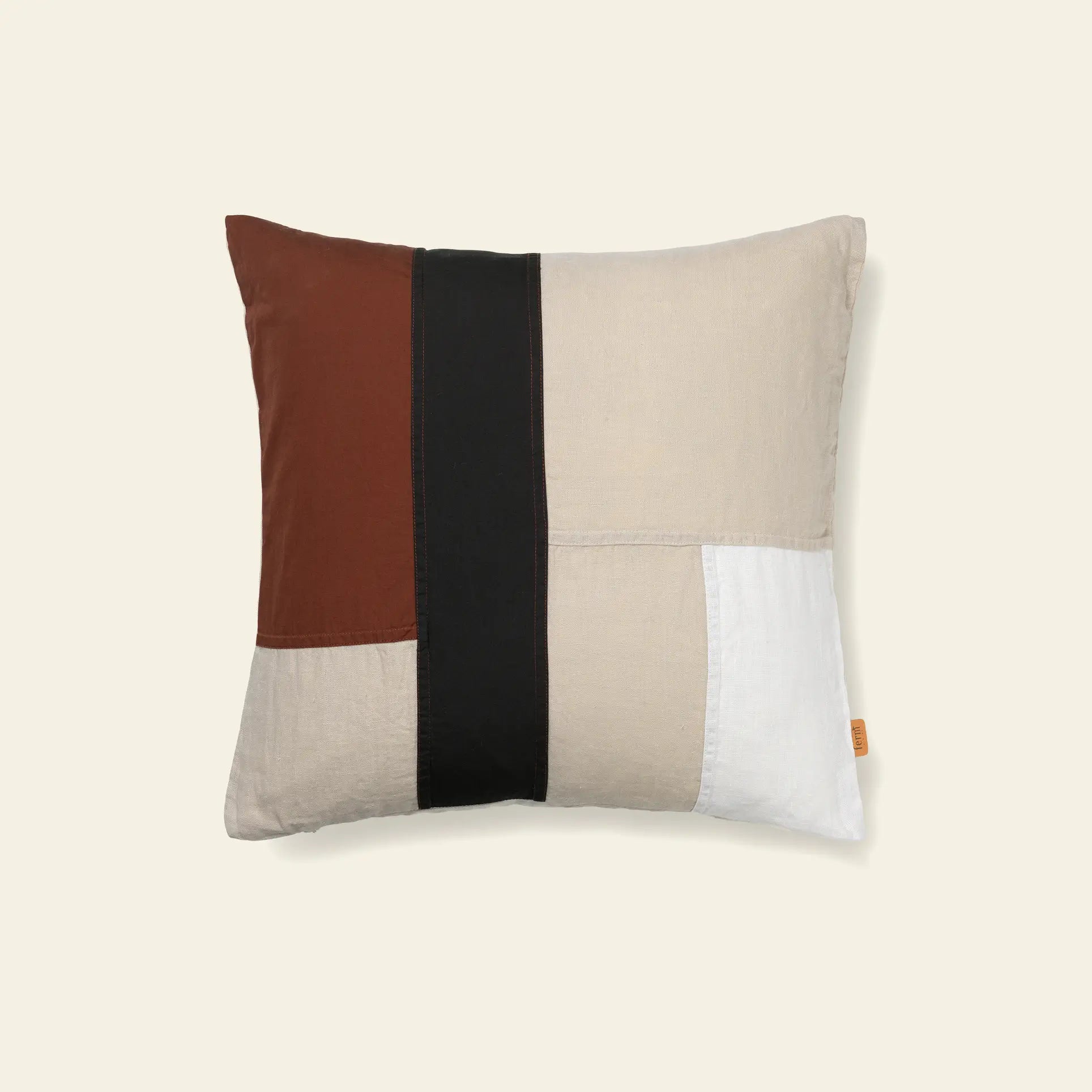The ferm LIVING Part Cushion by ferm LIVING features a square patchwork design in beige, brown, black, and white organic cotton, shown on a light cream background.