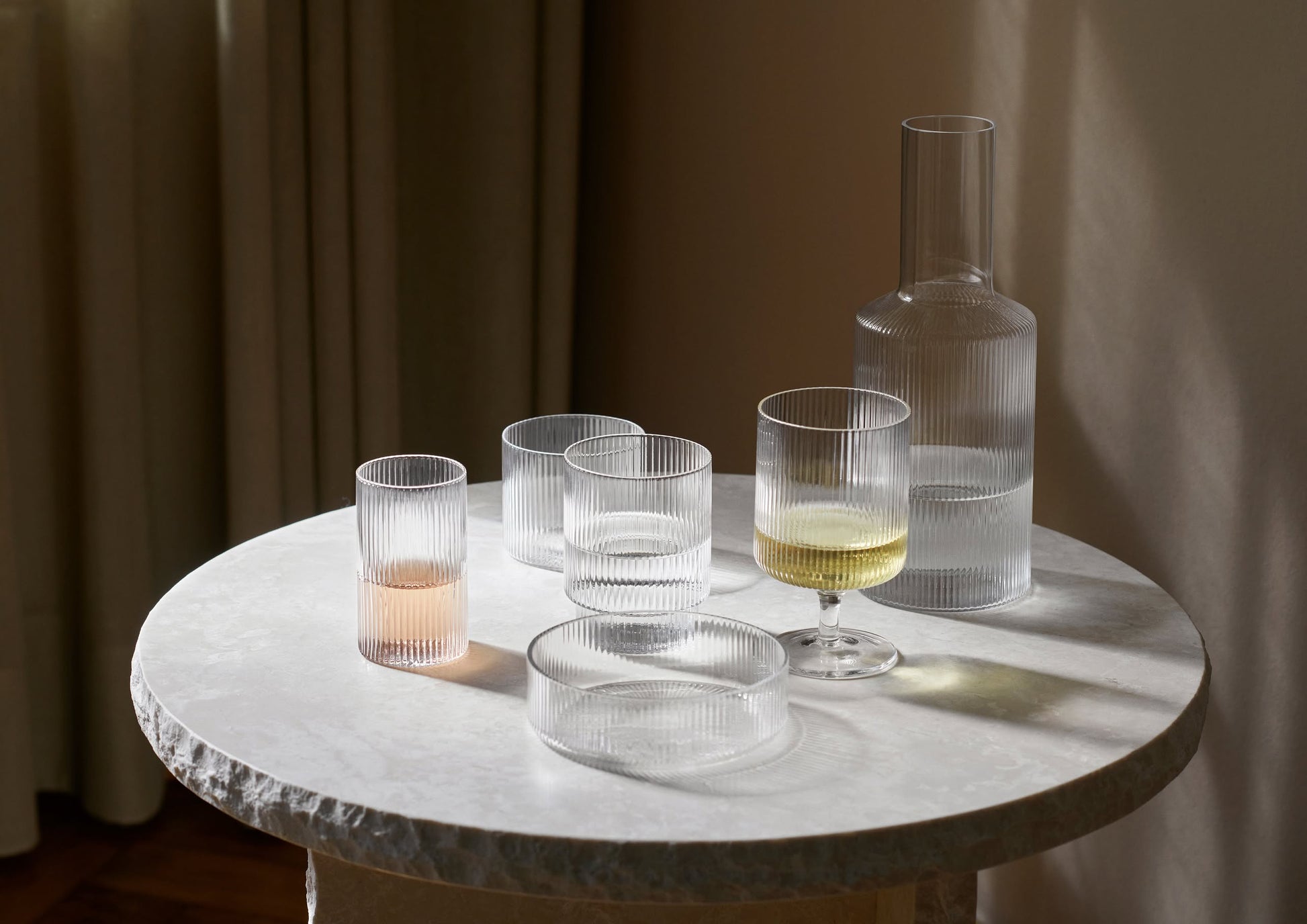 A round marble table displays a set of four ferm LIVING Ripple Serving Bowls. Soft light casts gentle shadows on the textured surface, enhancing the calm, minimalist atmosphere.