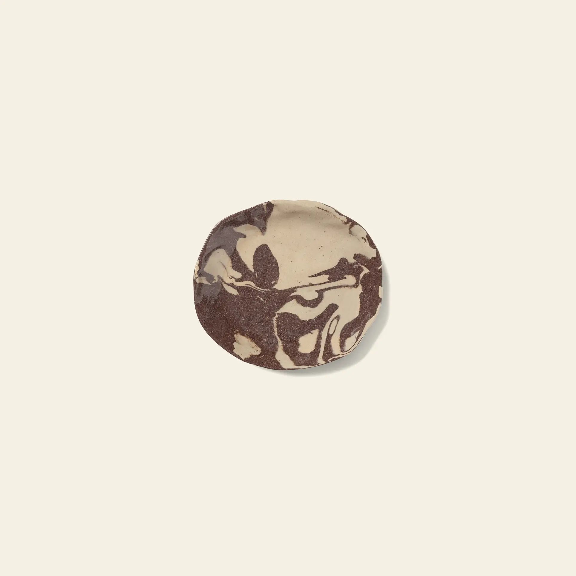A round cookie with marbled beige and brown swirls rests on an off-white surface, reflecting the Nerikomi-inspired patterns found in the ferm LIVING Ryu Platter, 18.5cm by ferm LIVING.