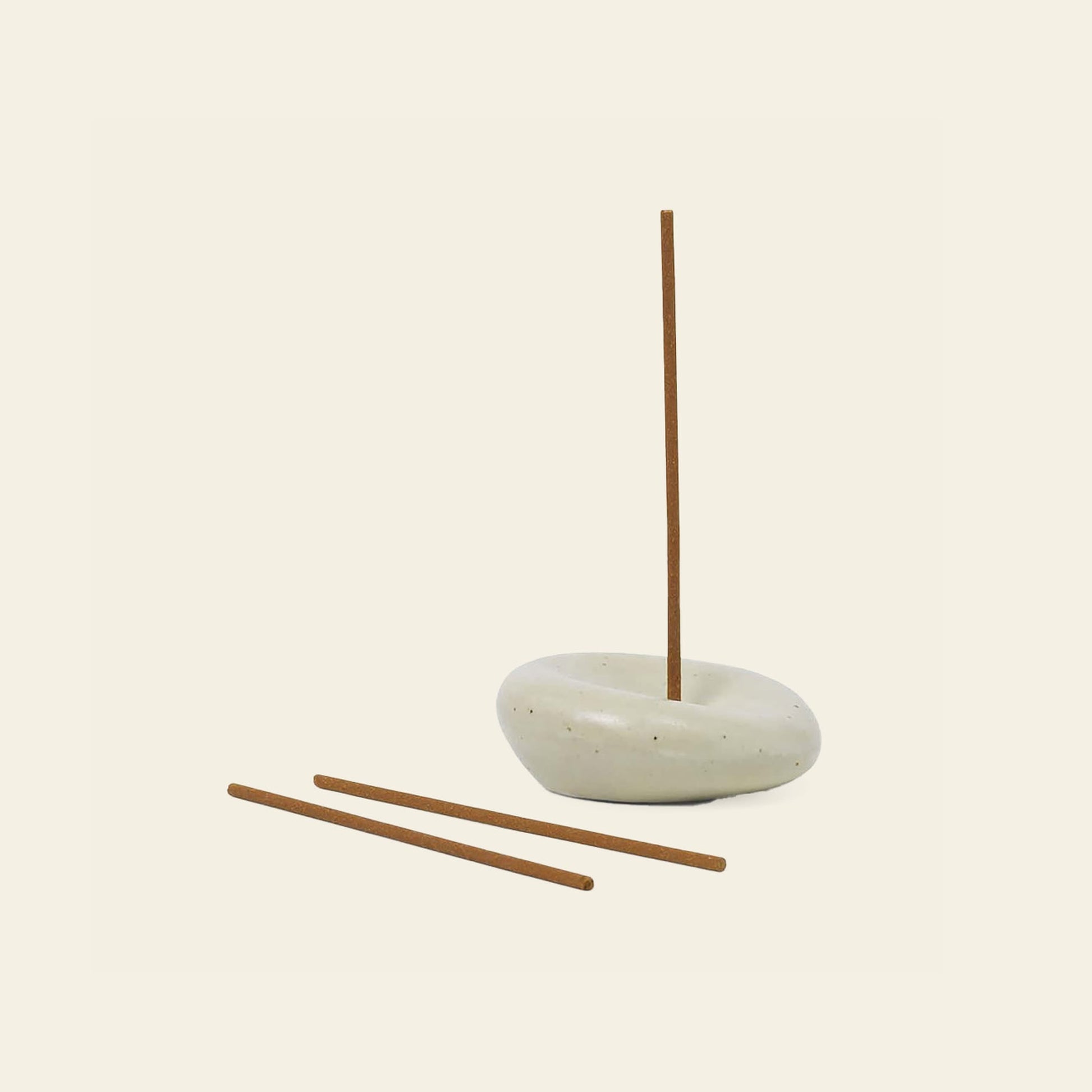 The ferm LIVING Sense Incense Holder Gift Set features a white, rounded ceramic holder displaying one upright sandalwood incense stick, with two extras lying in front—a calming gift set from ferm LIVING shown against a light background.