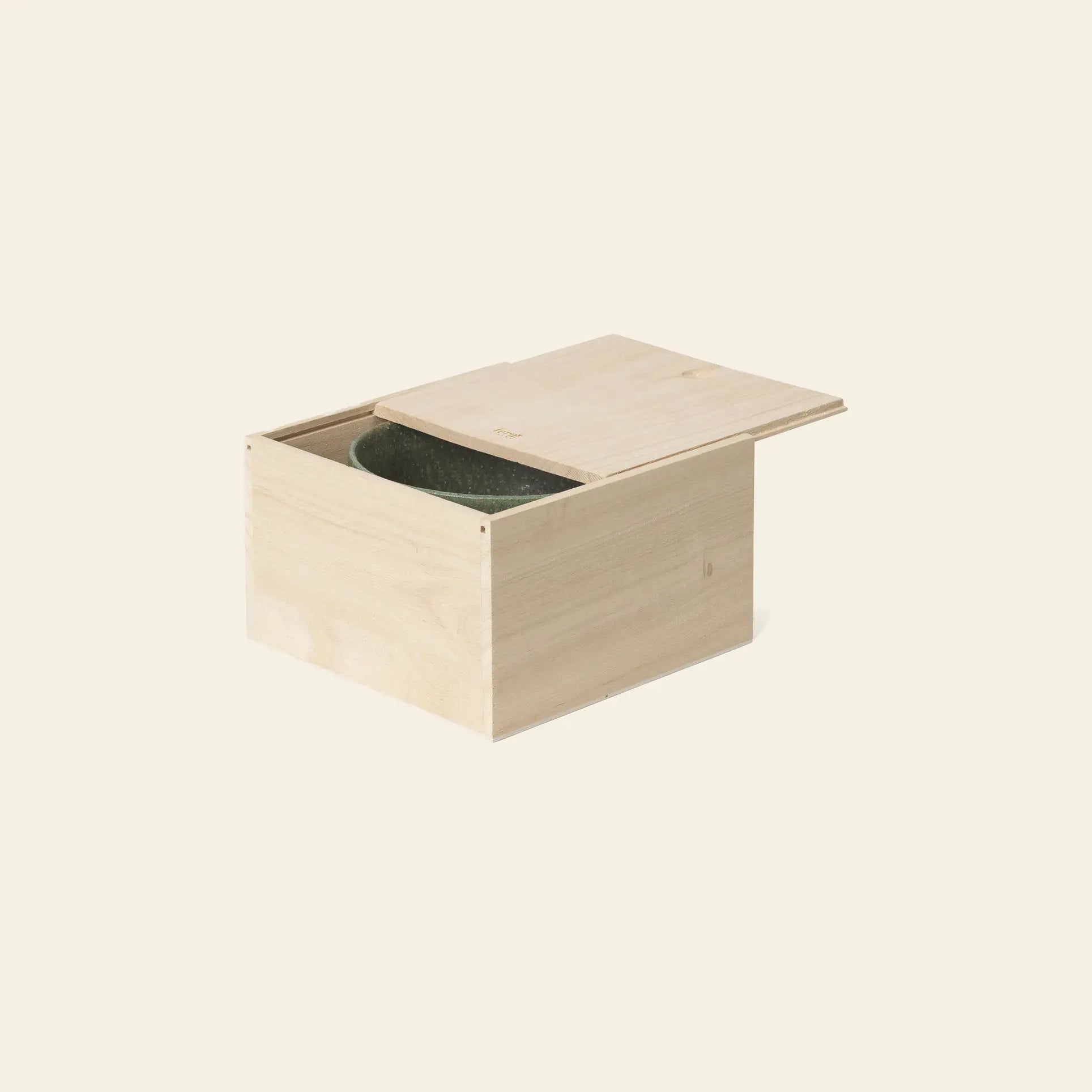 A light wooden box with a sliding lid, partially open to reveal the ferm LIVING Serena Bowl, 12.5cm, in green inside, set against a plain beige background.