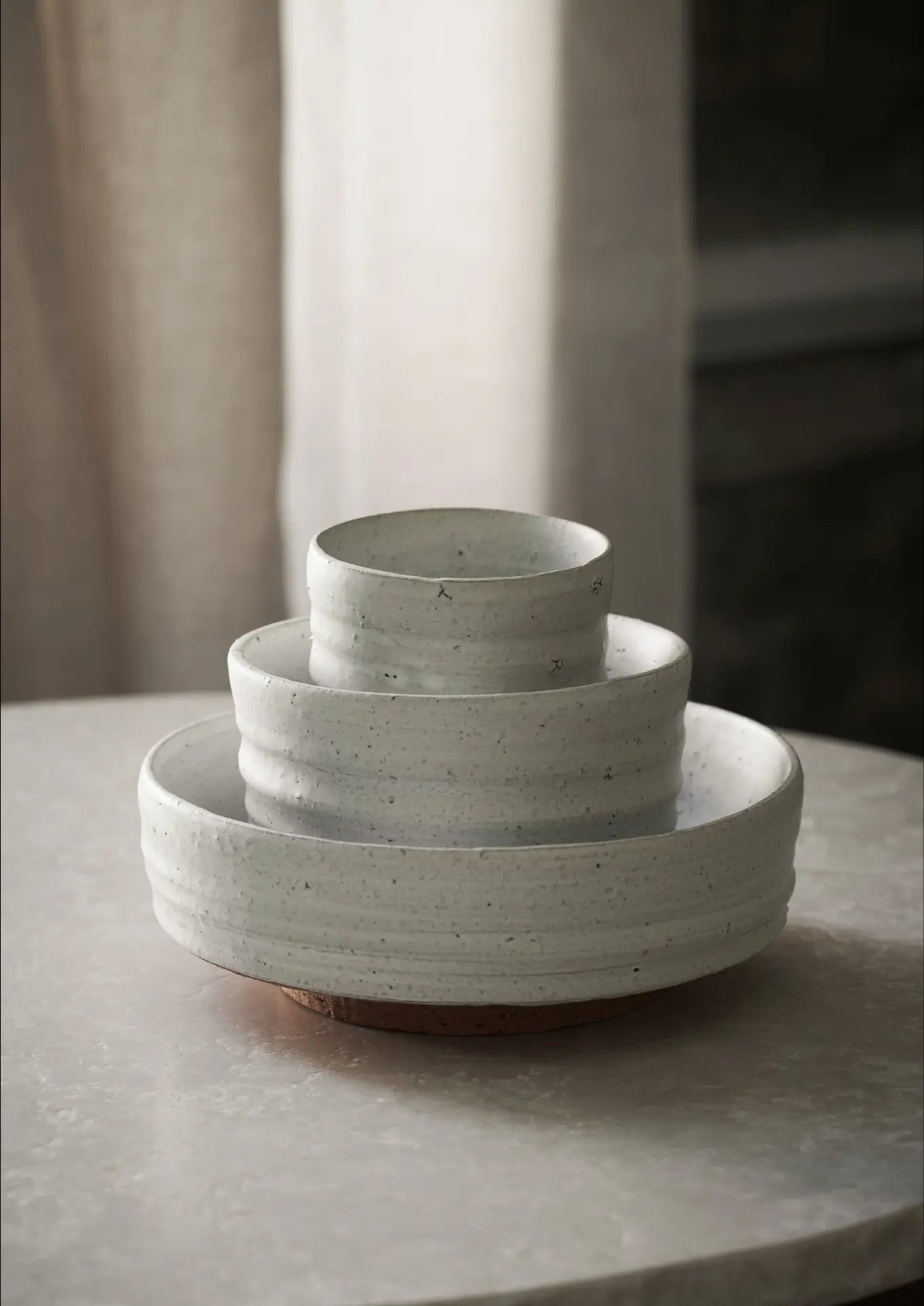 The ferm LIVING Serena Bowl, 12.5cm, showcases a minimalist white ceramic design and luxurious texture as it rests on a round, light marble surface with a gently lit neutral backdrop.