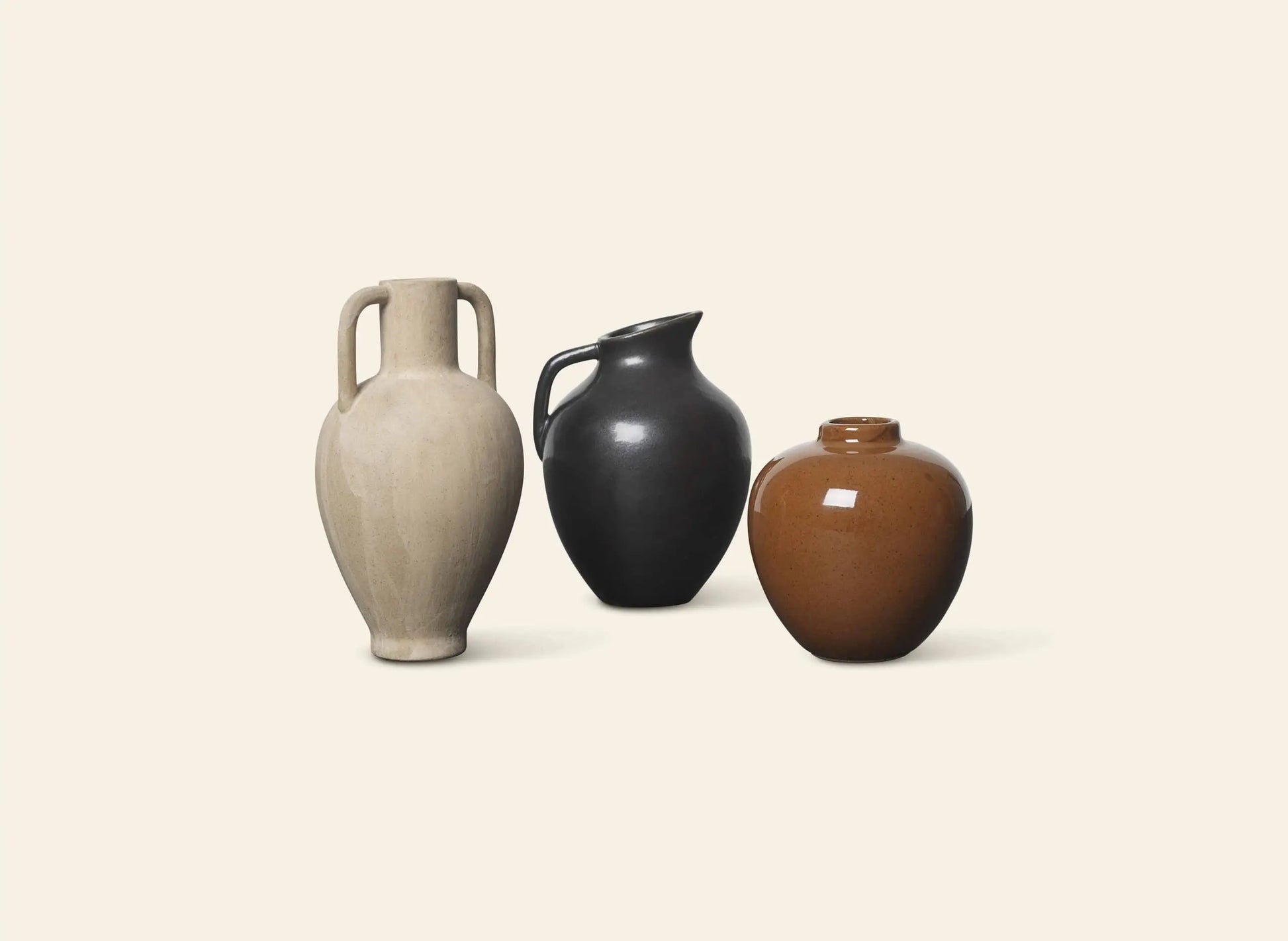 Three ceramic vases—including ferm LIVING Ary Mini Vase M in brown, a beige two-handled design, and a black spouted vase—are displayed on an off-white background, blending ancient Greek inspiration with modern style.