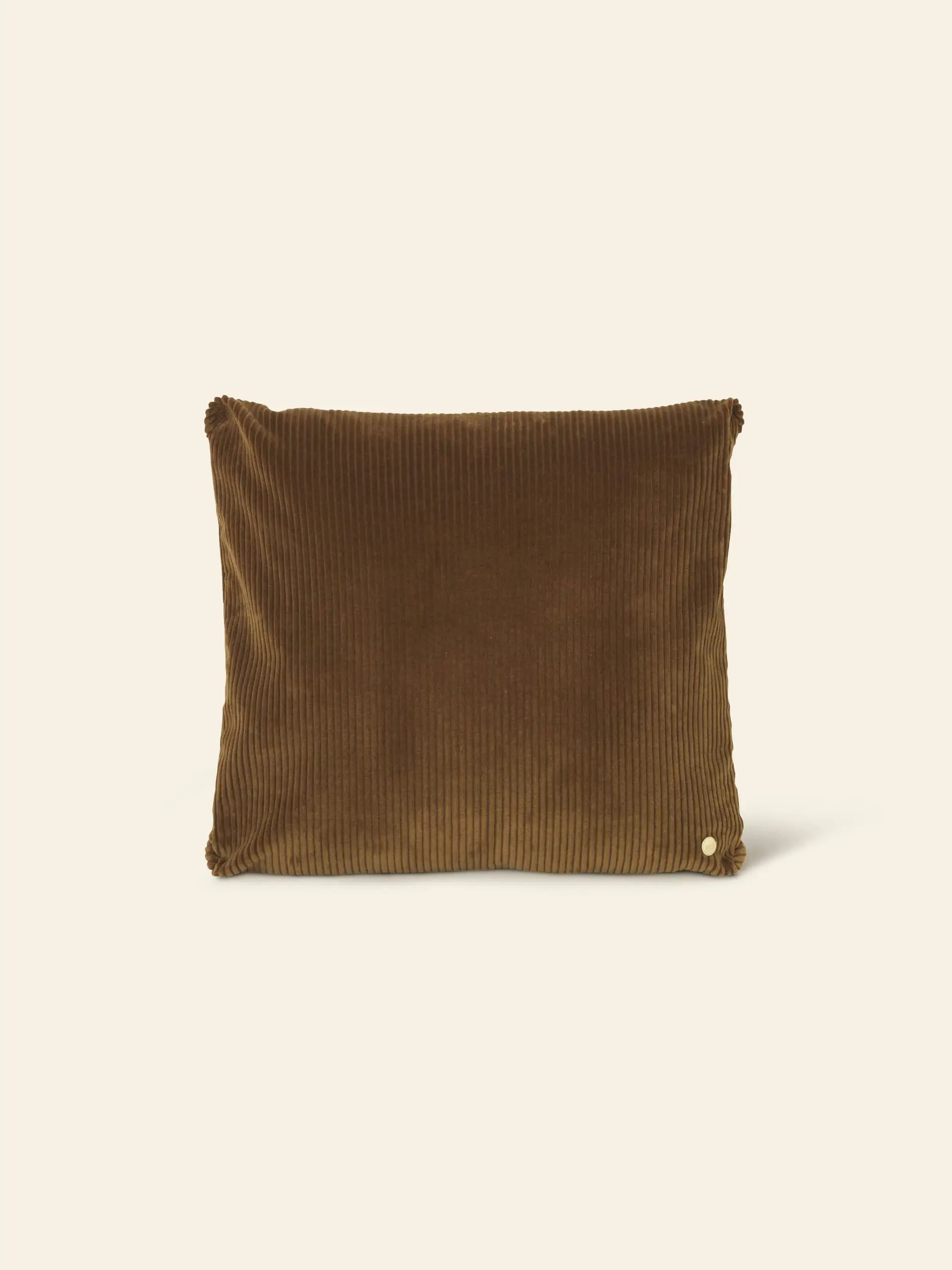 The ferm LIVING Corduroy Cushion is a rectangular brown pillow featuring a subtle ribbed texture and a small round button, adding understated luxury to any space. Shown here against a plain beige background.
