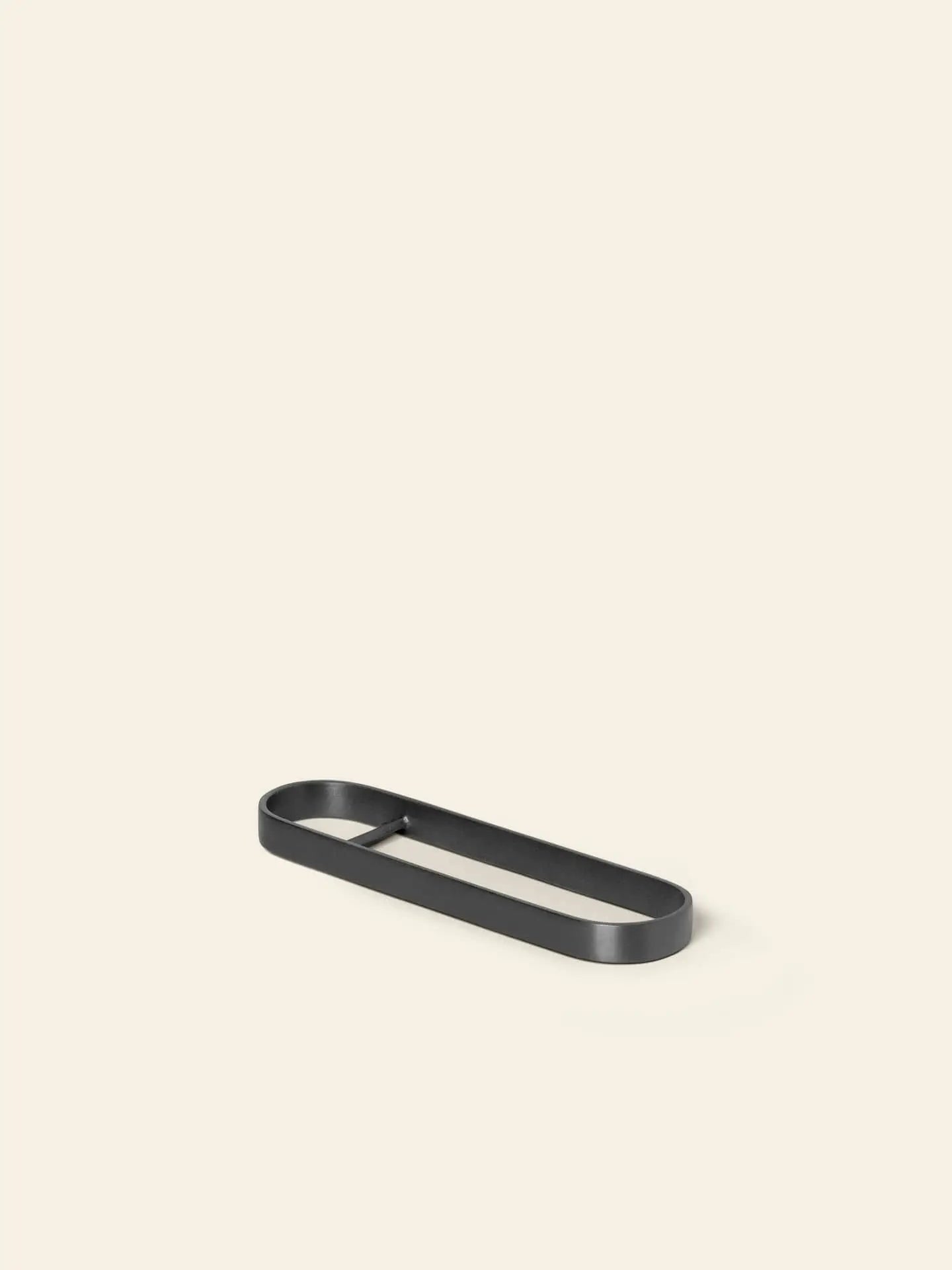 The ferm LIVING Fein Bottle Opener by ferm LIVING, featuring a minimalist black metal design with an oval shape and low edge, is displayed on a plain light beige background—perfect for a contemporary kitchen.
