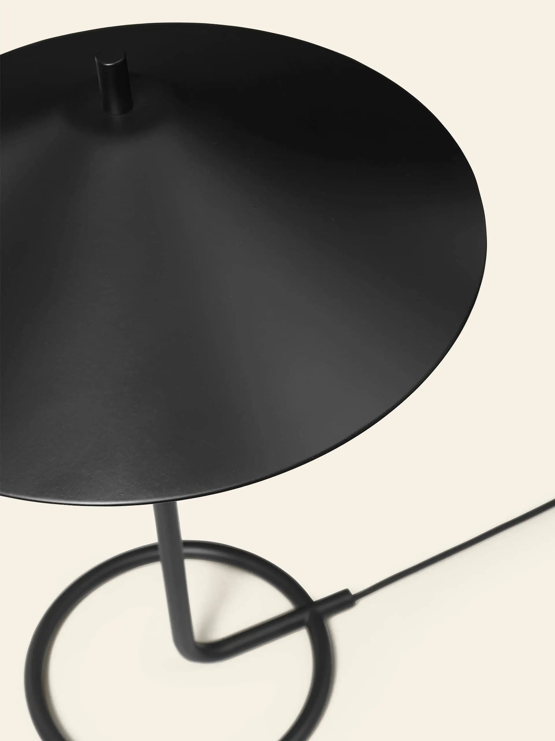 The ferm LIVING Filo Table Lamp in black powder-coated iron features a wide, conical shade and circular base. Perfect for modern spaces, it sits on a light beige background with its power cord extending to the right.