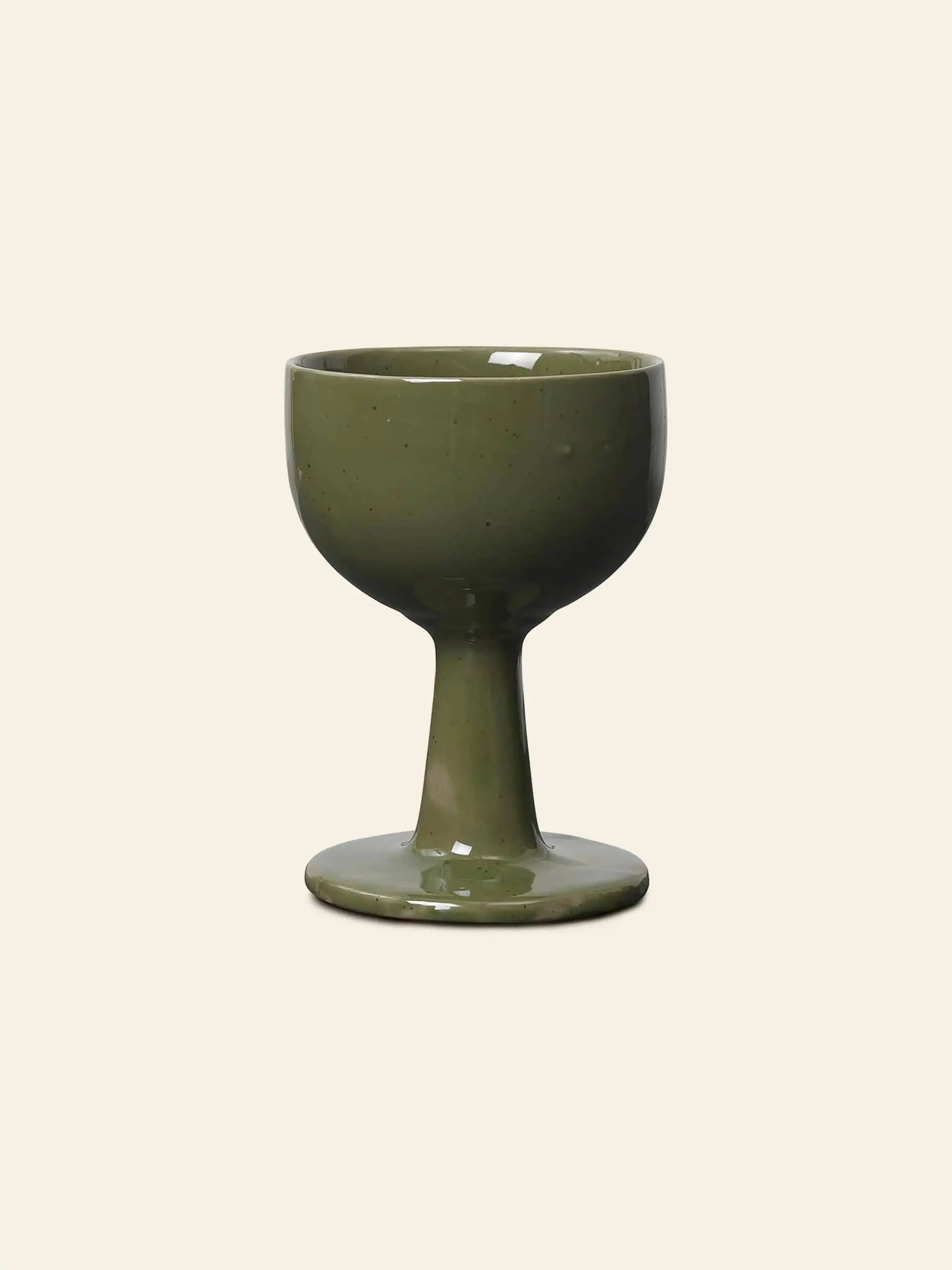 The ferm LIVING Floccula Wine Glass by ferm LIVING features green ceramic with a wide bowl and thick stem, evoking cozy French bistros, set against a plain beige background.
