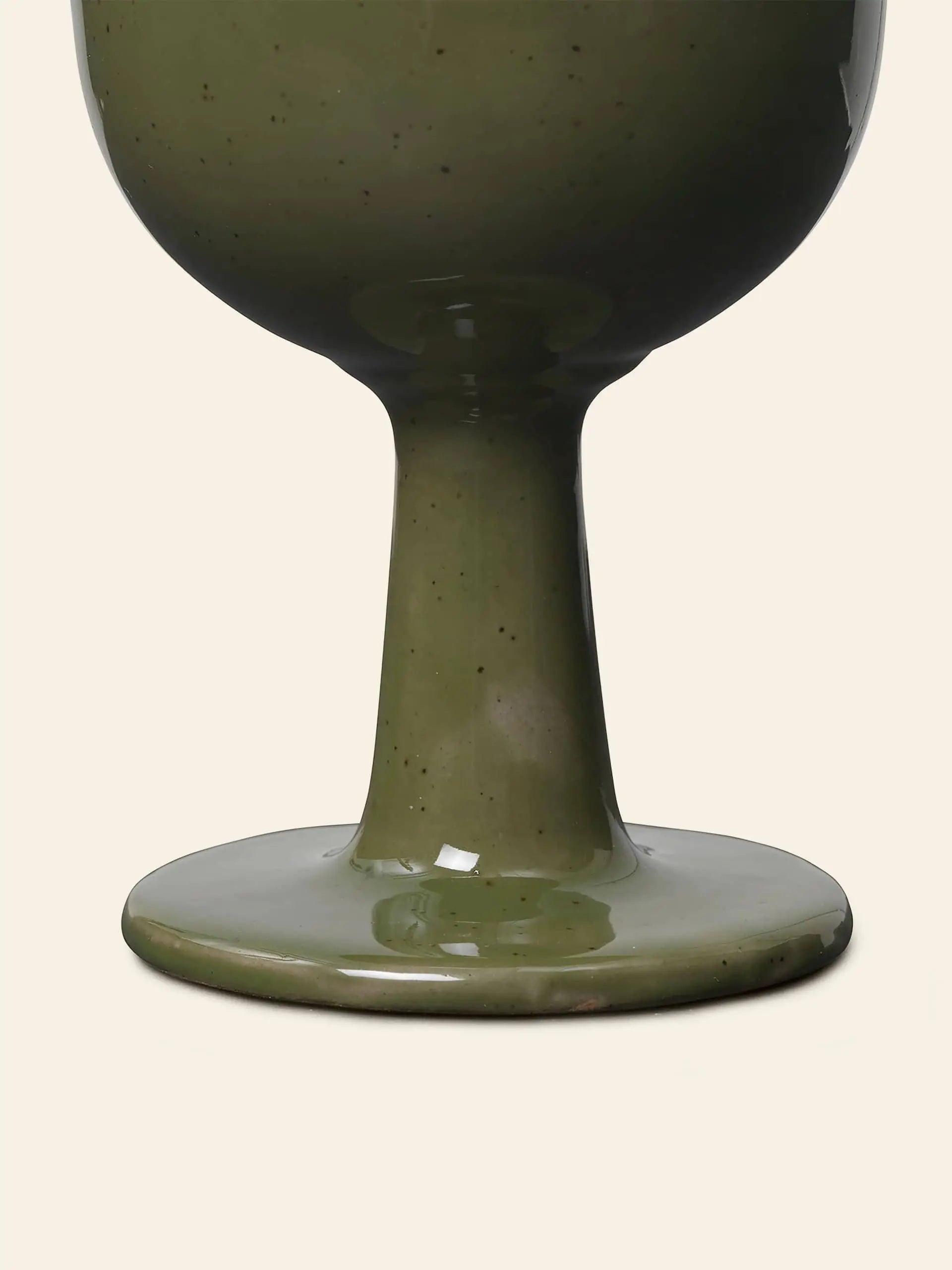 A close-up of the base and stem of the ferm LIVING Floccula Wine Glass by ferm LIVING, featuring green ceramic with a glossy finish against a plain beige background—capturing French bistro charm.