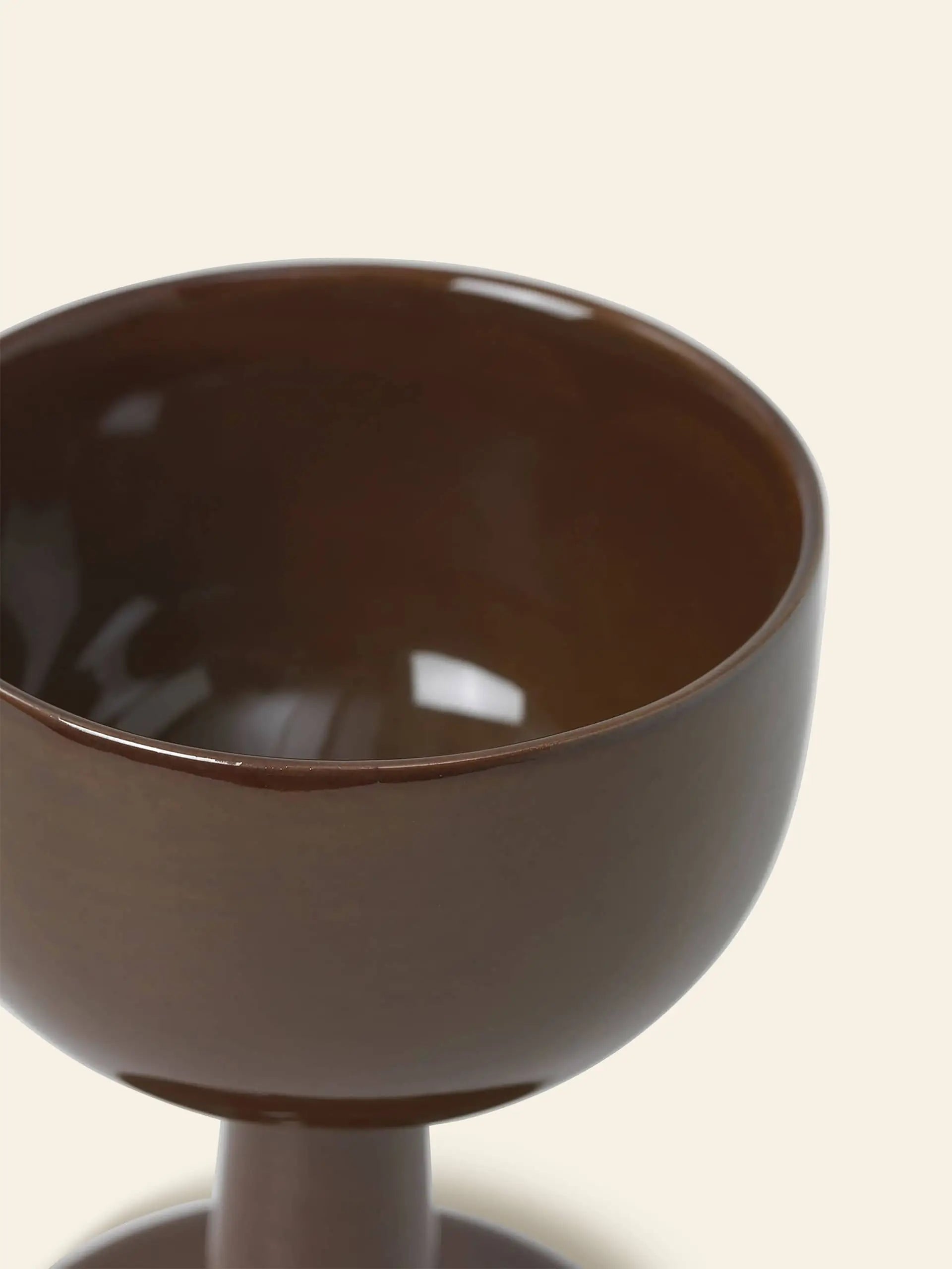 Close-up of the ferm LIVING Floccula Wine Glass by ferm LIVING, featuring a glossy dark brown ceramic finish. Only the upper half and part of the stem are shown against a simple light-colored background.