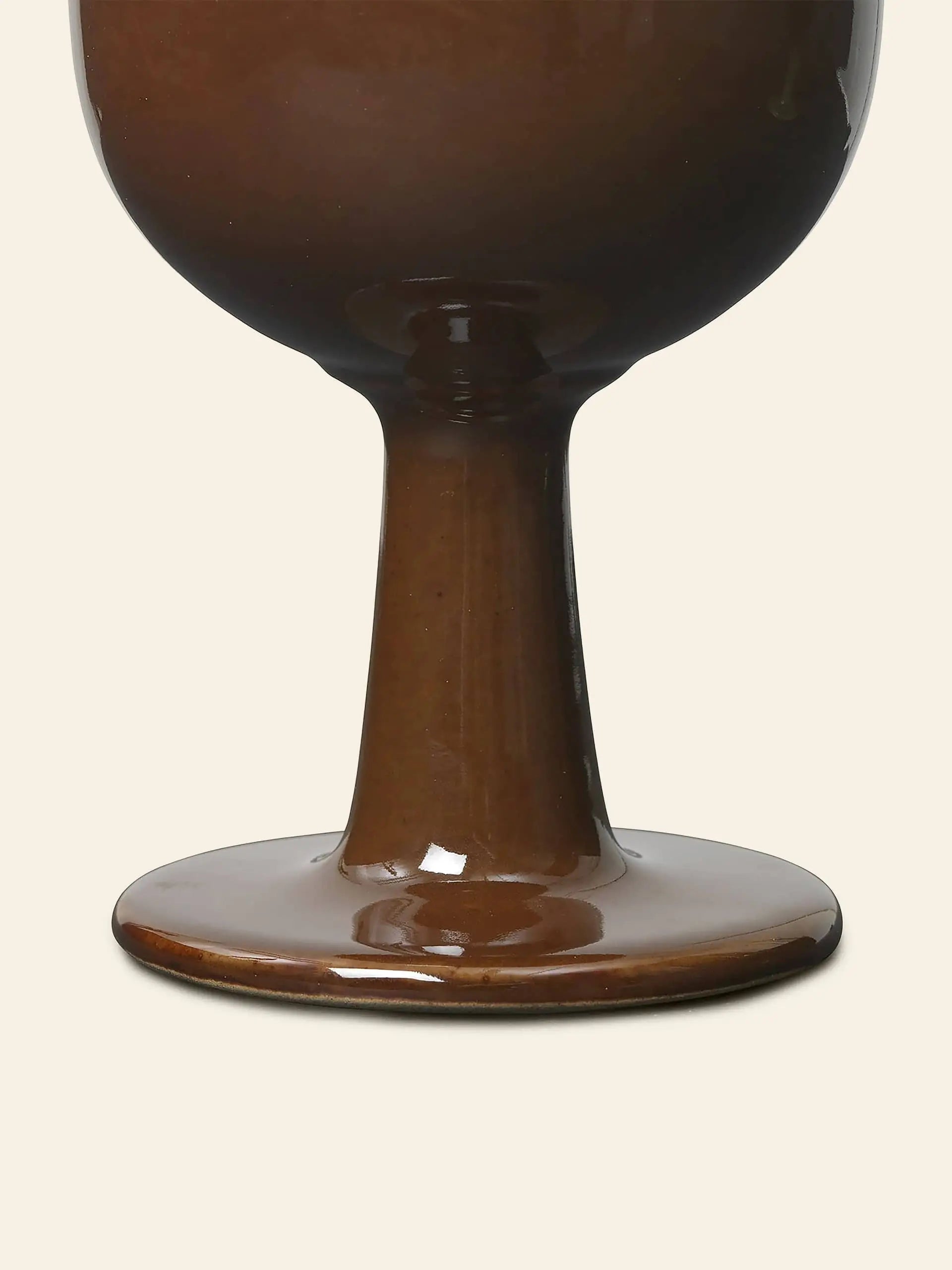 Close-up of the base and stem of the glossy brown ferm LIVING Floccula Wine Glass, set against a plain, light beige background.