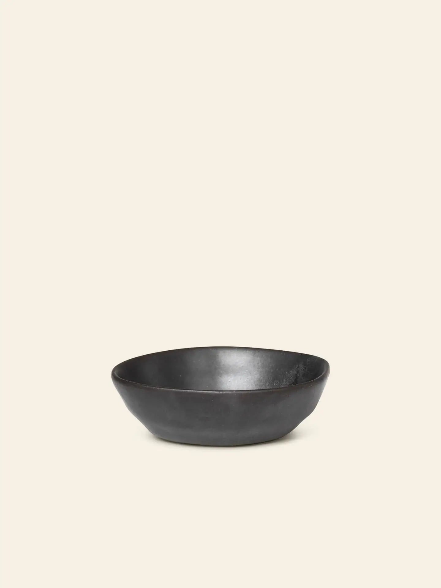 A small black Flow Porcelain Bowl by ferm LIVING is centered on a plain beige background, highlighting stylish and refined artisanal tableware.