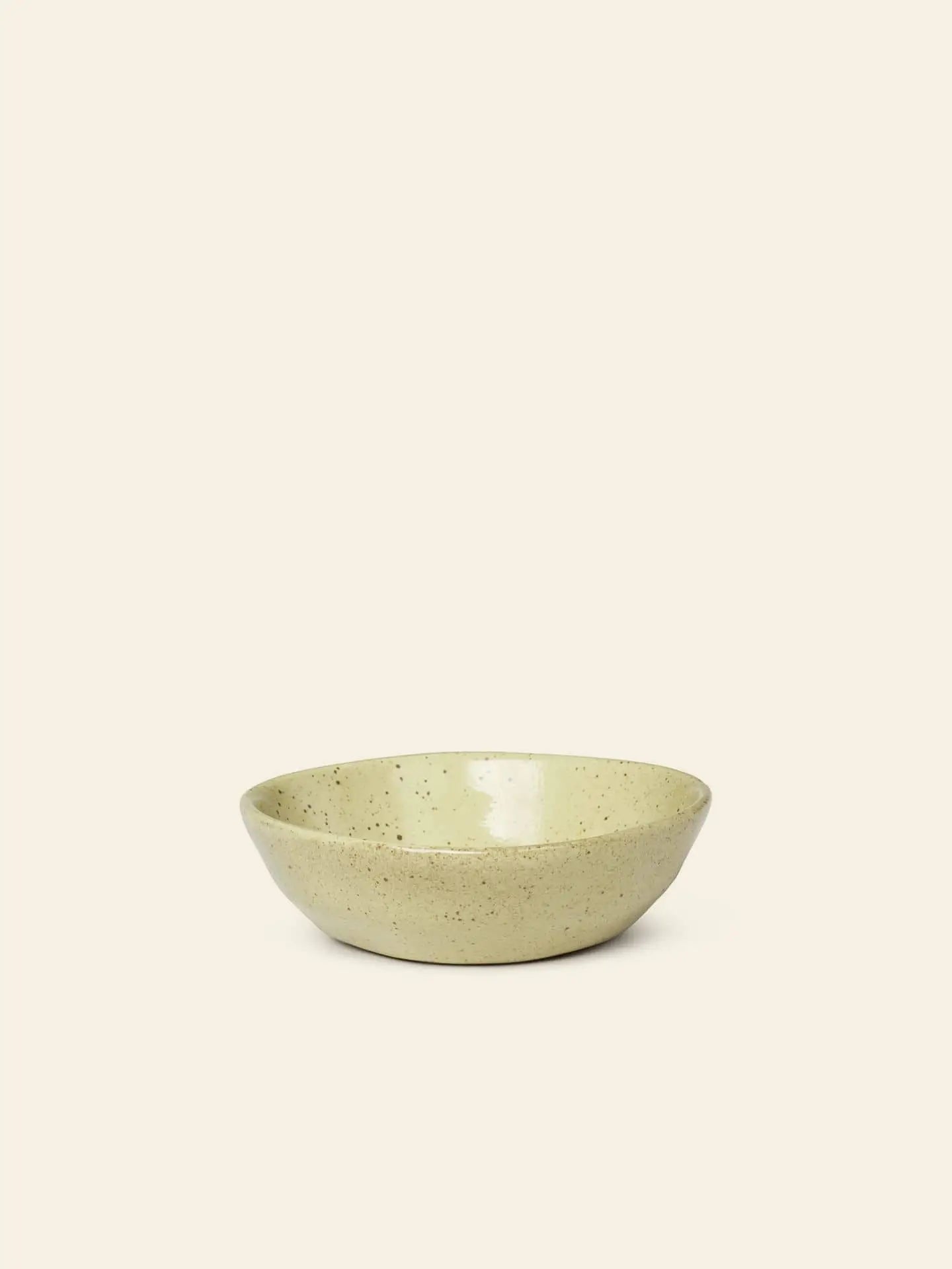 The ferm LIVING Flow Porcelain Bowl, Small, features a shallow, round shape and beige speckled finish, adding an artisanal touch to any table setting.