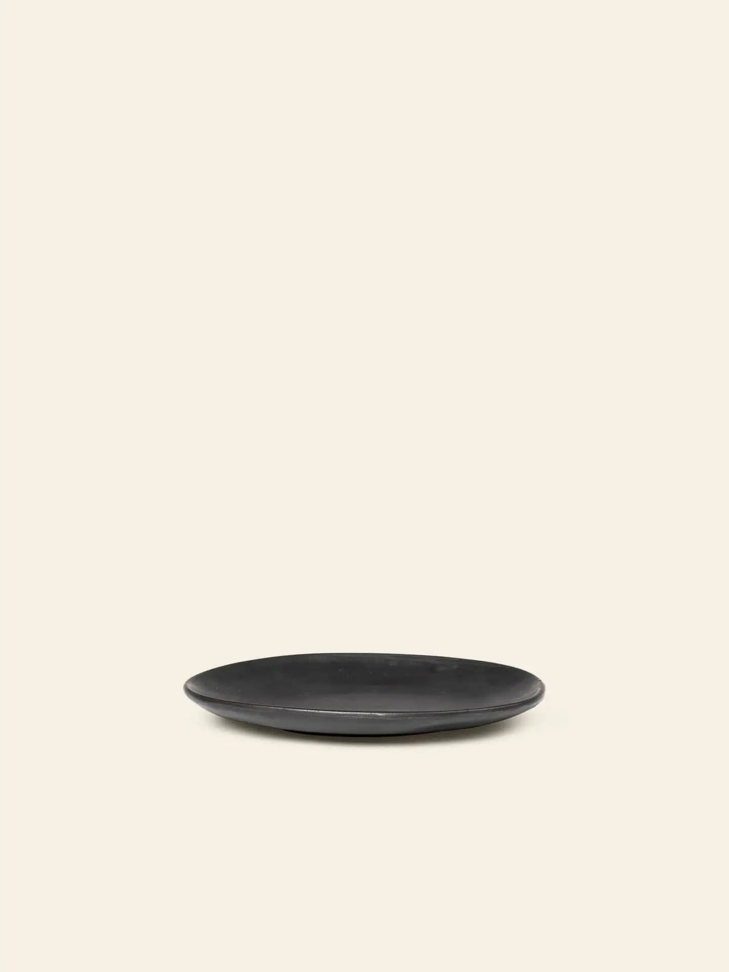 The ferm LIVING Flow Plate, Small—a simple round black porcelain plate by ferm LIVING—rests on a plain light beige background with ample empty space above.