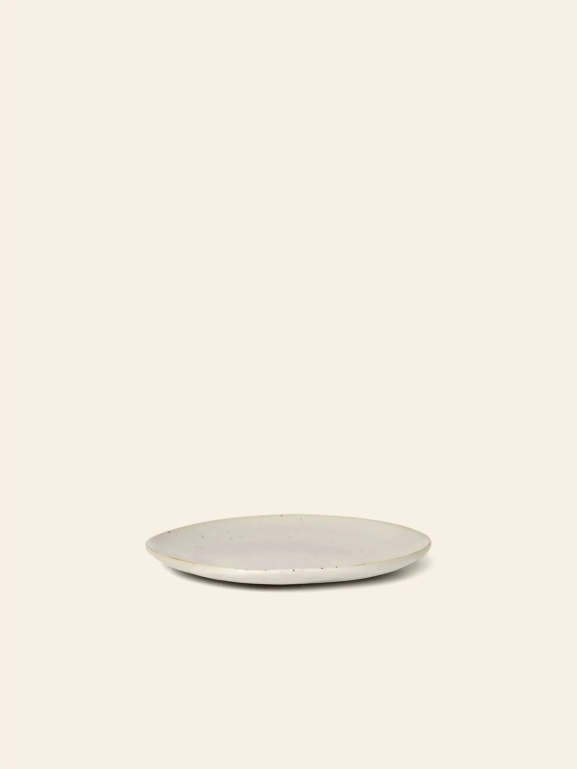 The ferm LIVING Flow Plate, Small, features a simple round porcelain design with a light reactive glaze, shown centered on a plain beige background with no other objects present.