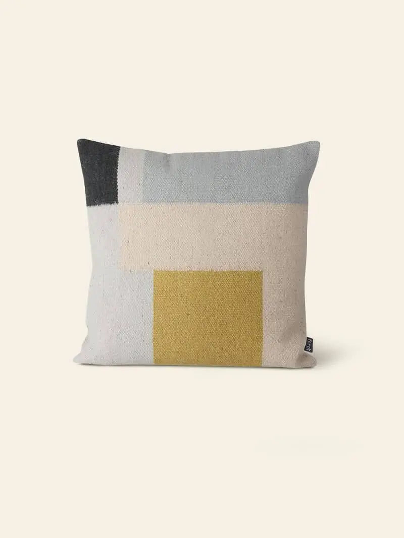 The ferm LIVING Kelim Cushion features a rectangular geometric design with blocks of black, light blue, beige, and mustard yellow on a light beige background—ideal for adding color to any Scandi-inspired space.