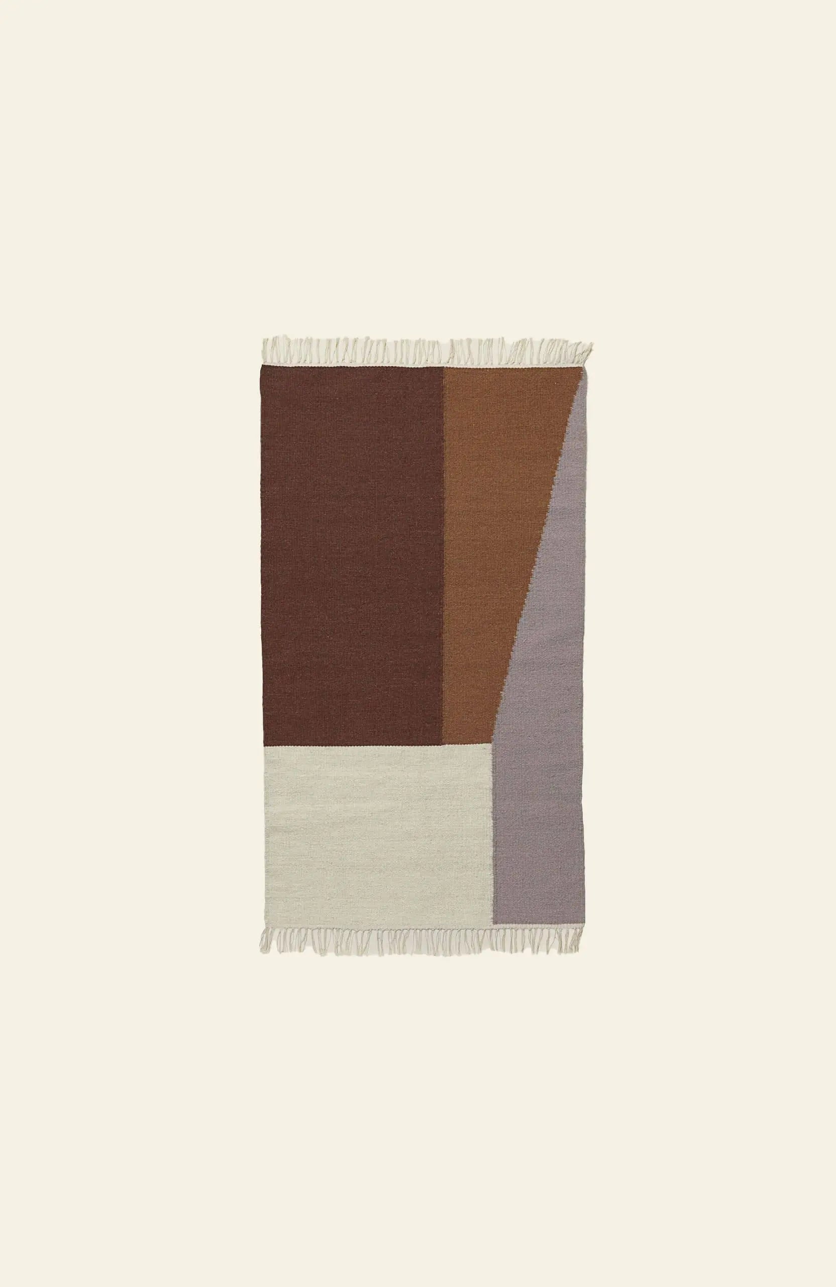 The ferm LIVING Kelim Rug is rectangular with an abstract geometric pattern in brown, tan, cream, and gray, plus fringe on the top and bottom edges. Its bold shapes create visual interest against a plain light background.